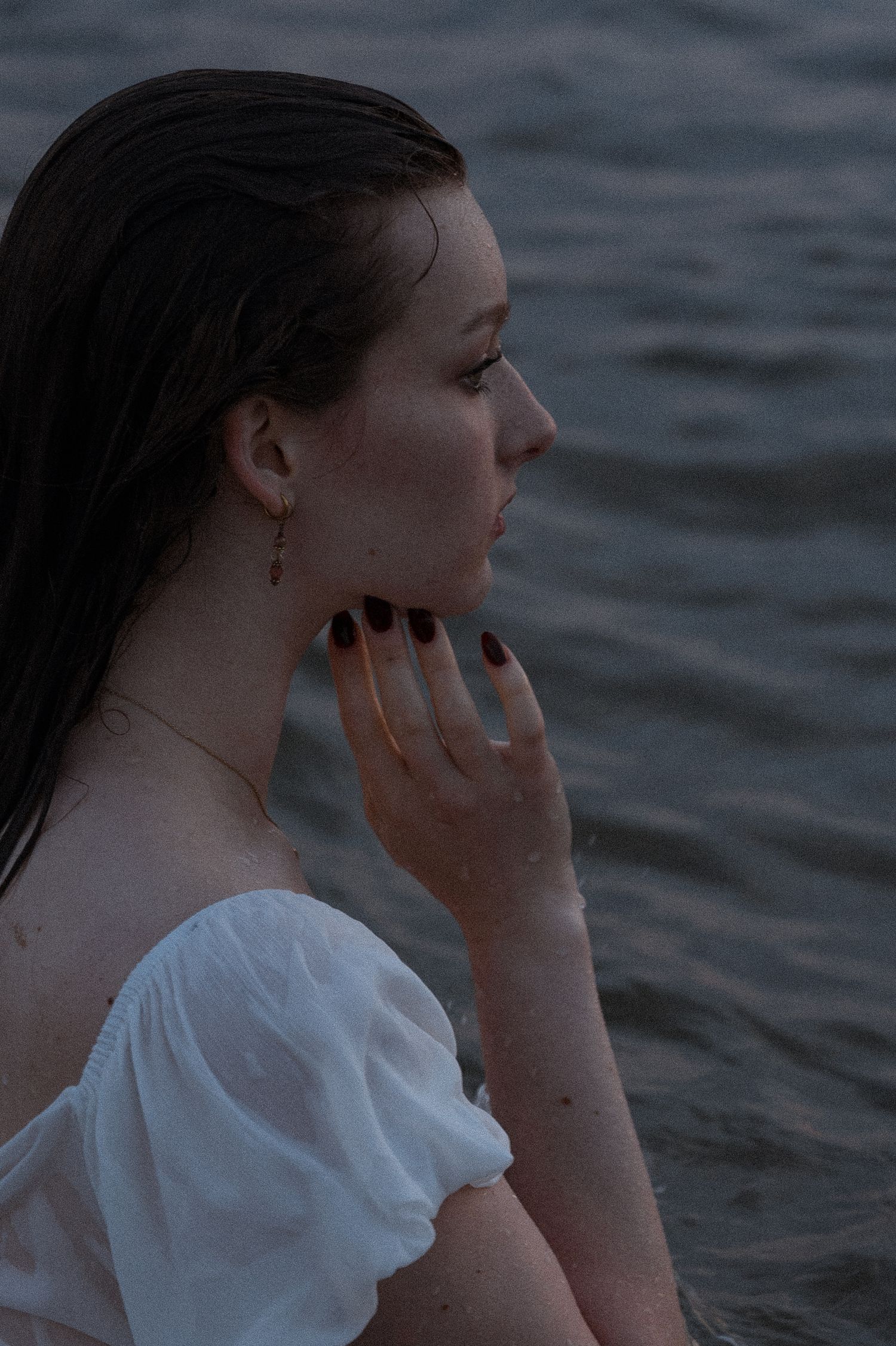 Contemplative portrait by the water wearing white during blue hour.