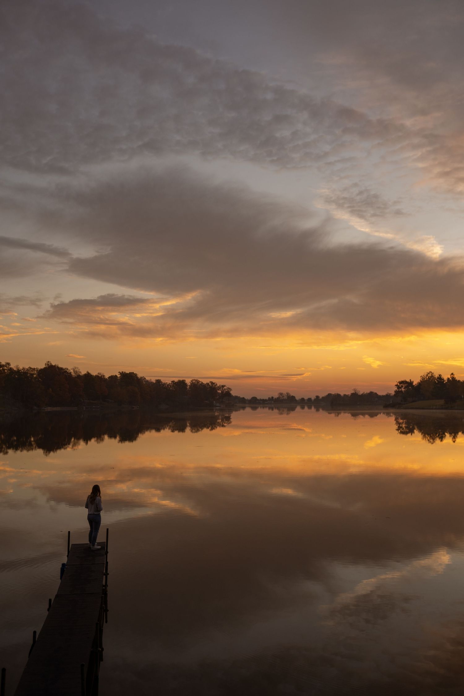 Tranquil sunset over a lake with silhouetted figures on a dock against an orange and purple sky.
