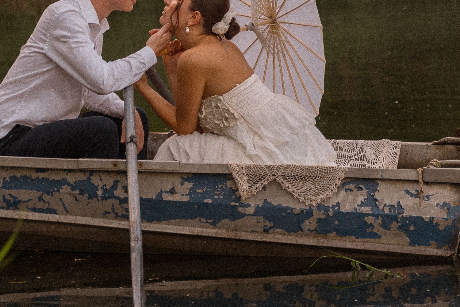 Couple sharing intimate moment in vintage rowboat with decorative parasol.