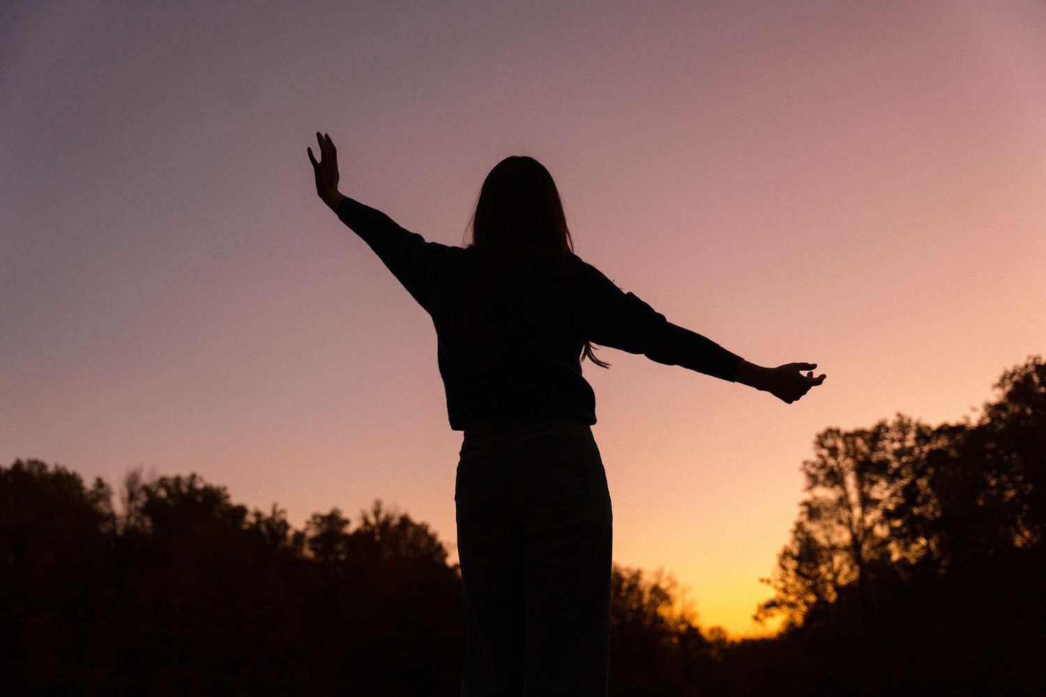 Silhouettes against a purple sunset sky with arms outstretched in joyful poses.