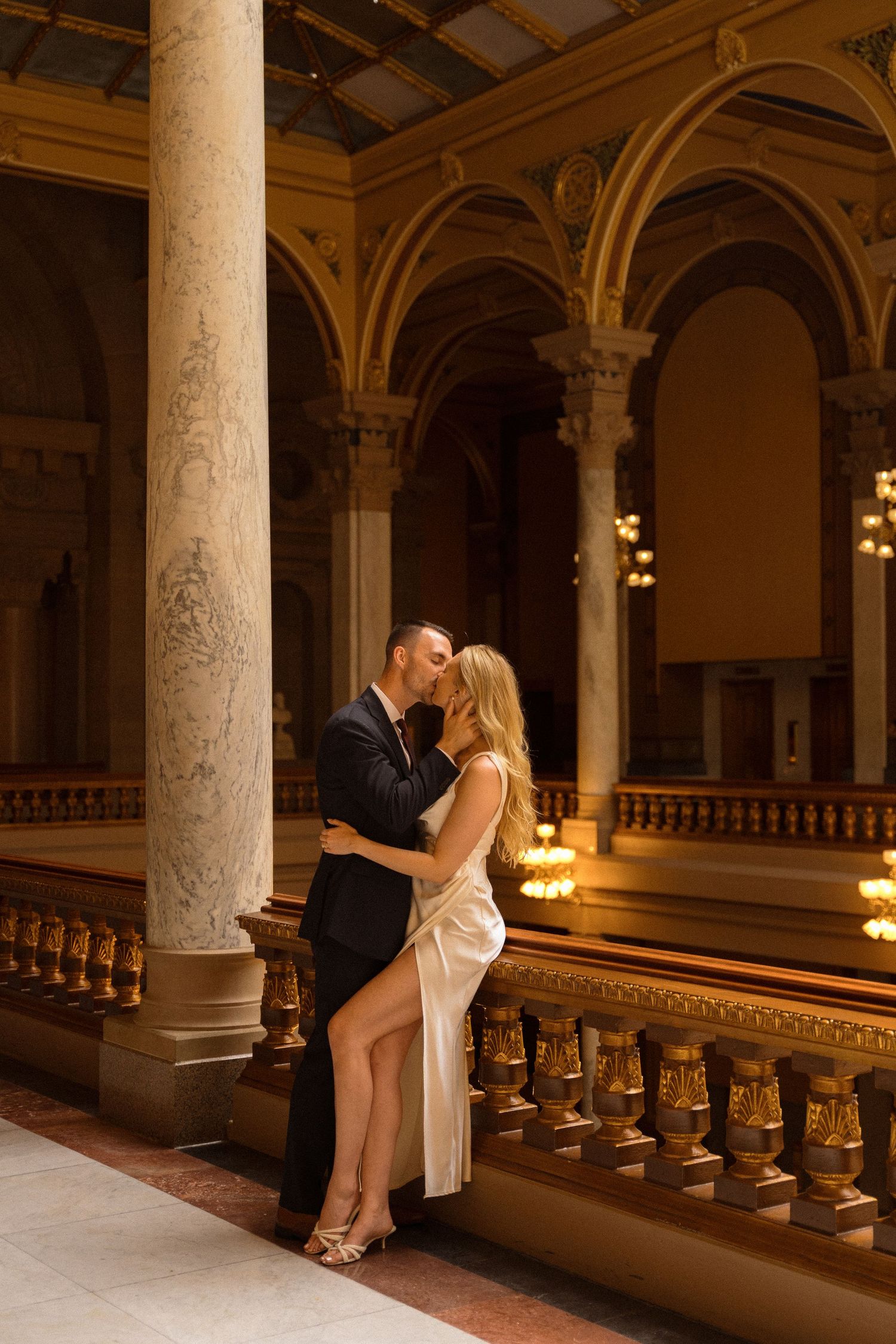 Elegant couple posing in a historic building with ornate columns and arches.