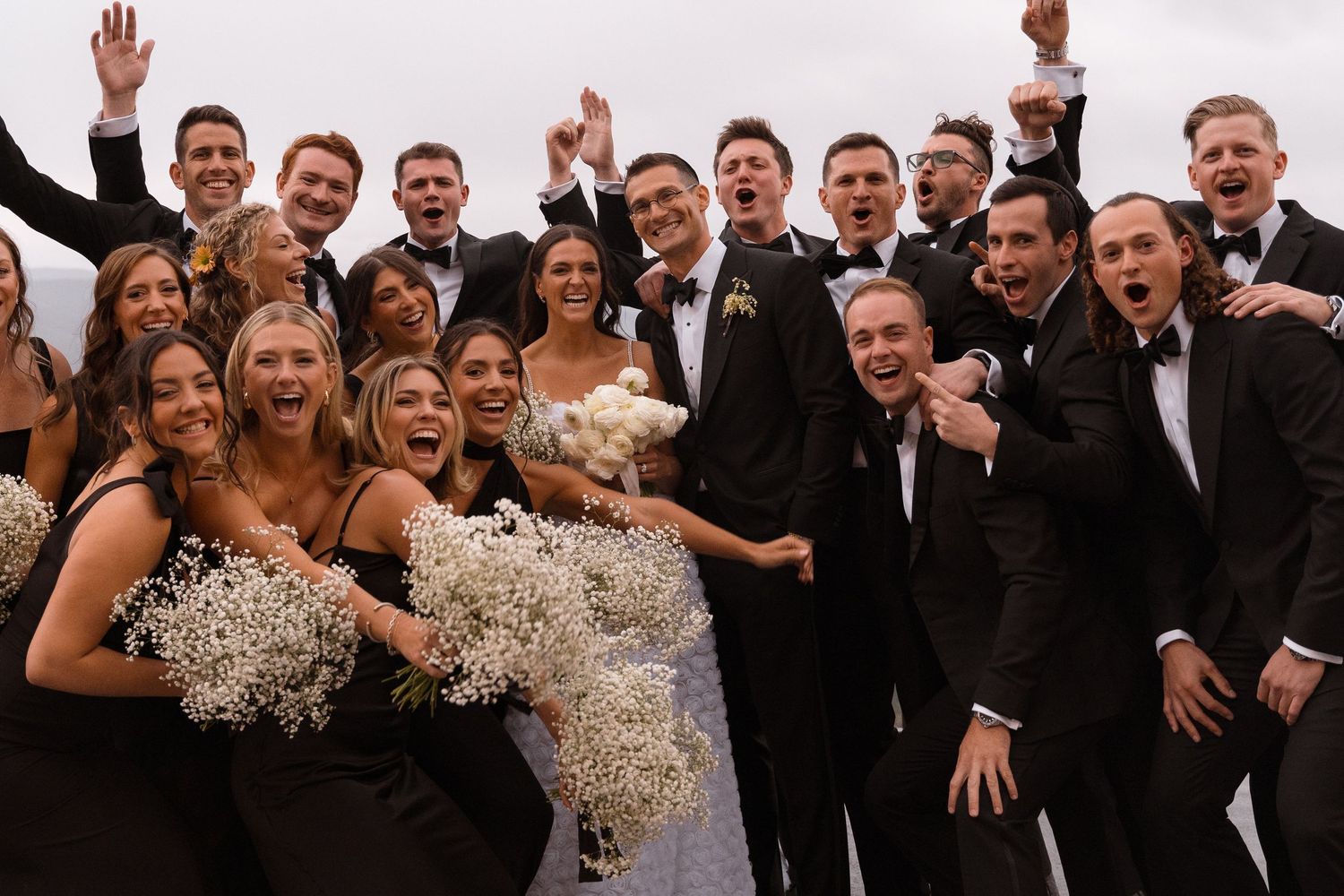 Large wedding party celebrating with raised arms and joyful expressions.