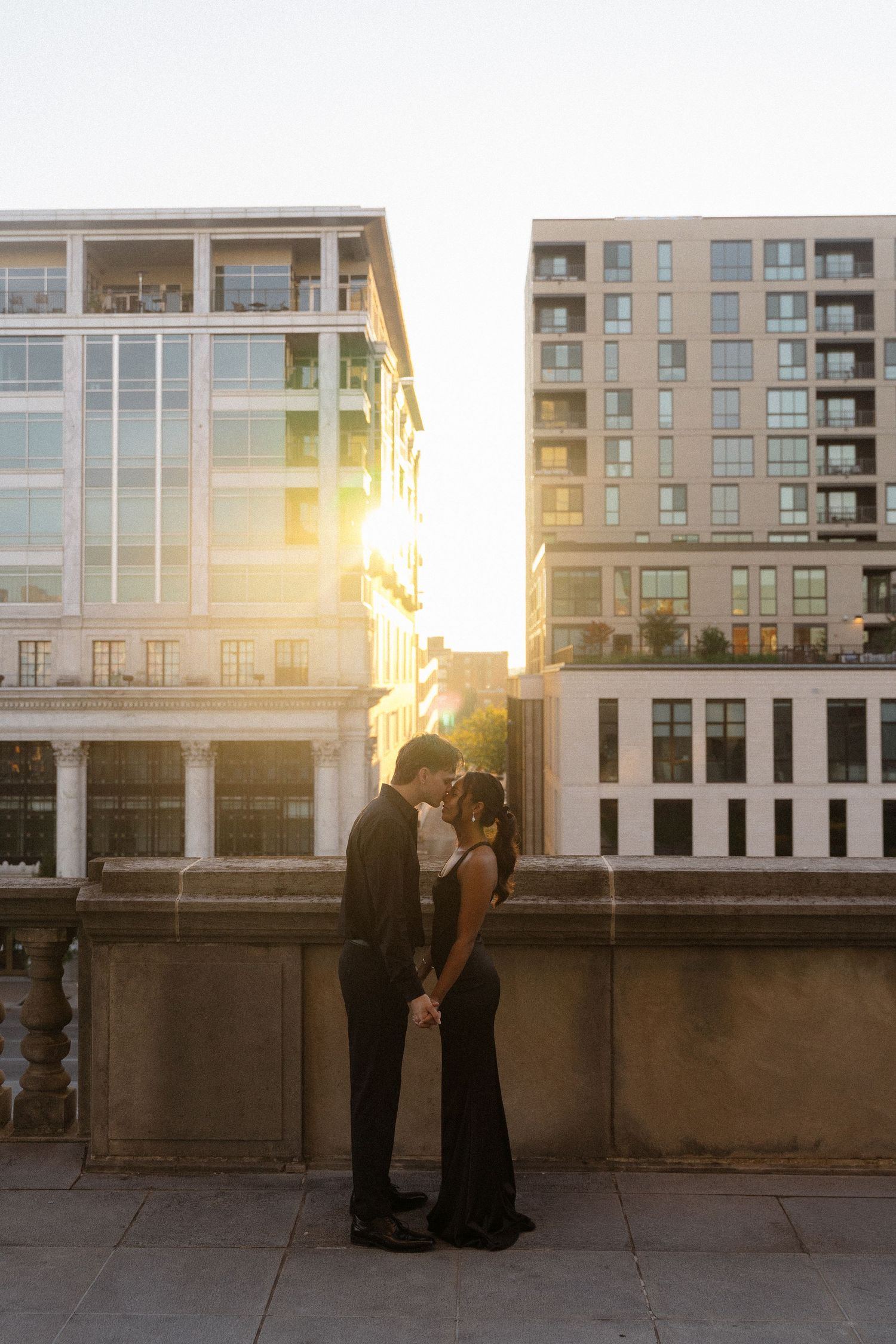Romantic silhouettes stand against modern apartment buildings at sunset creating a dramatic urban scene.
