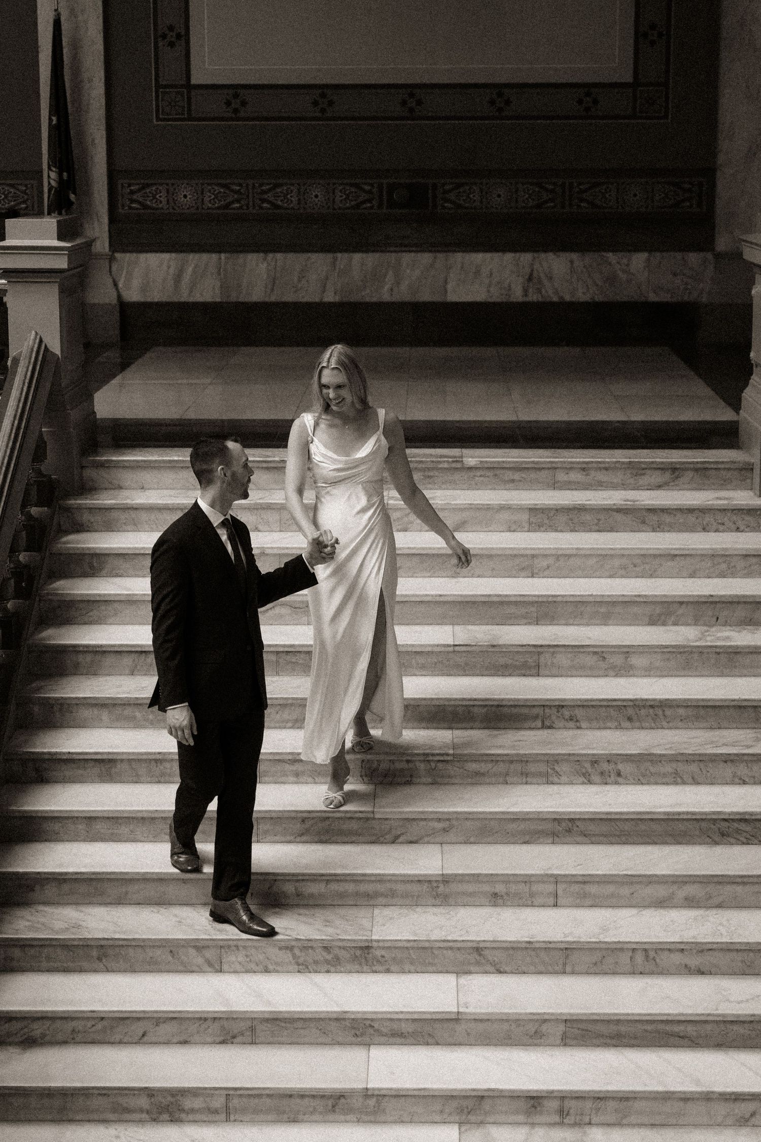 Black and white sequence of a couple walking up marble stairs in formal attire.