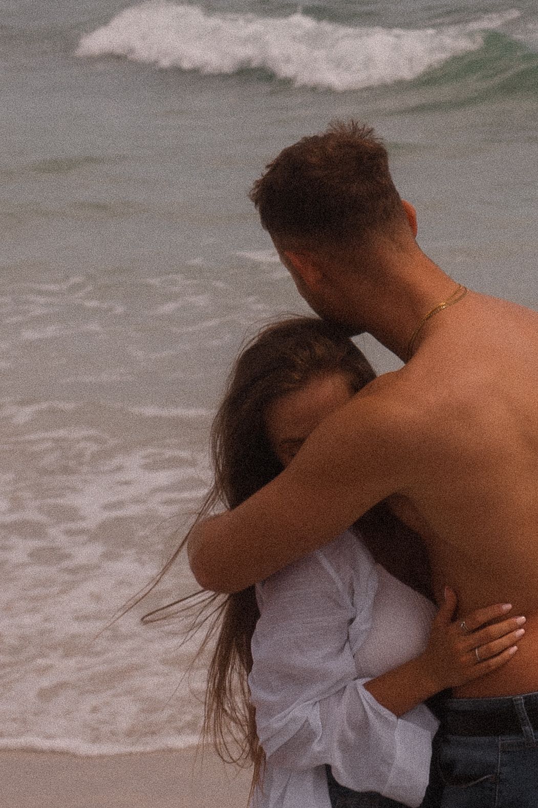 Couple embracing on beach with crashing waves in background.