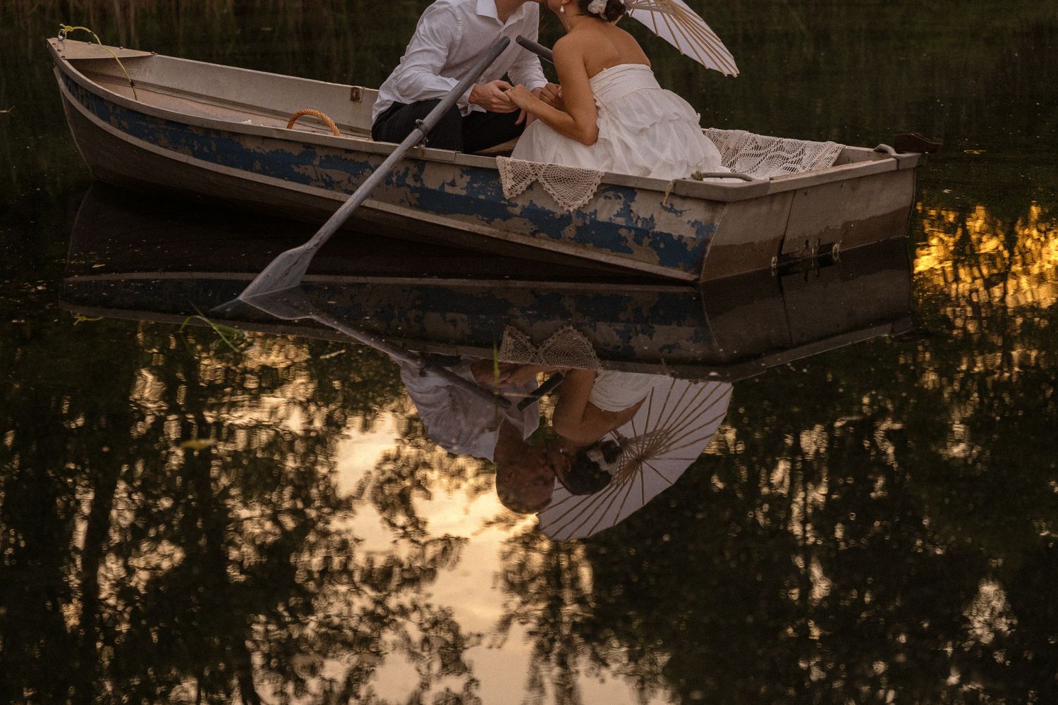 Peaceful lake scene at sunset with couple in wooden boat.