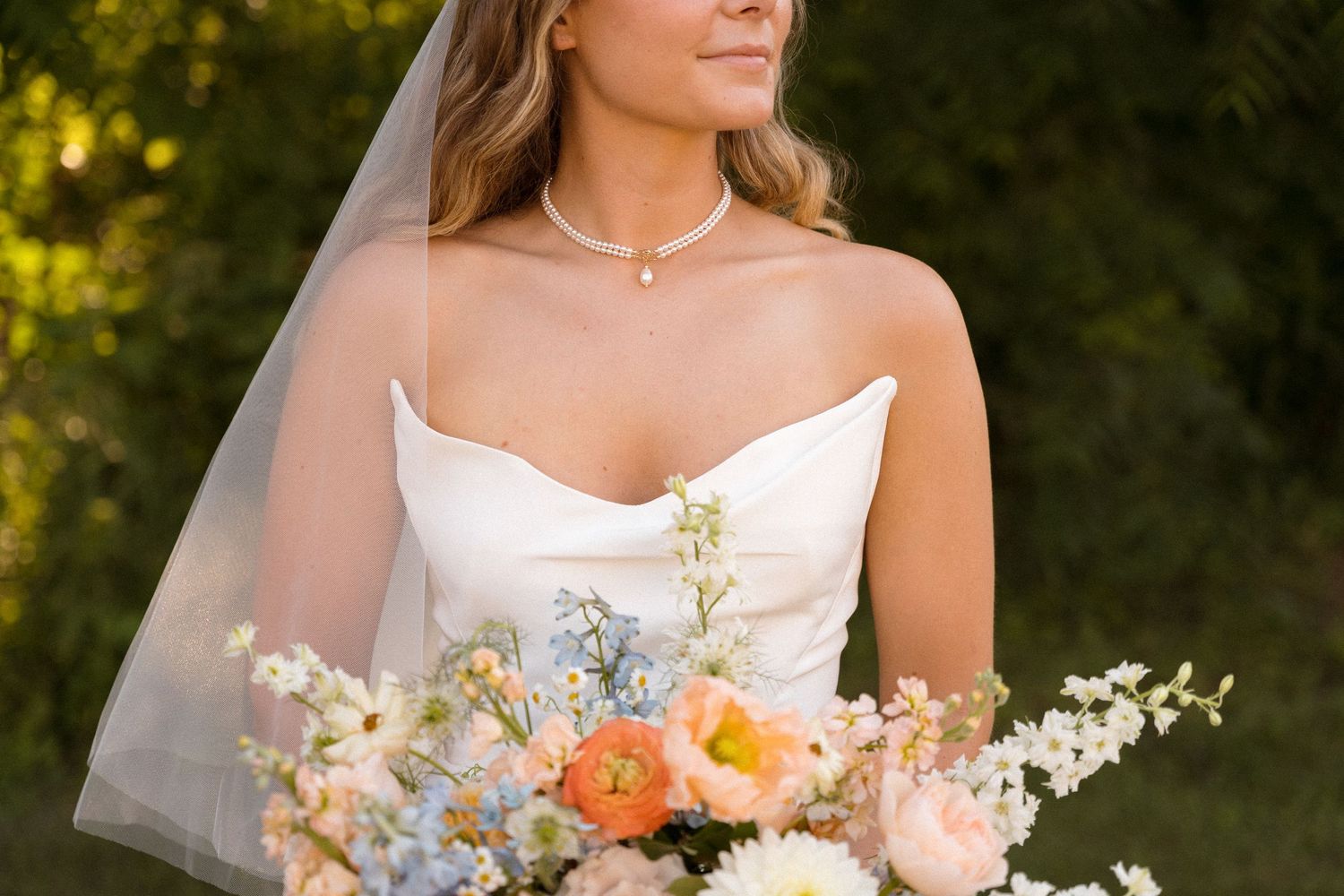 Elegant bridal bouquet with white, peach and blue flowers against natural background.
