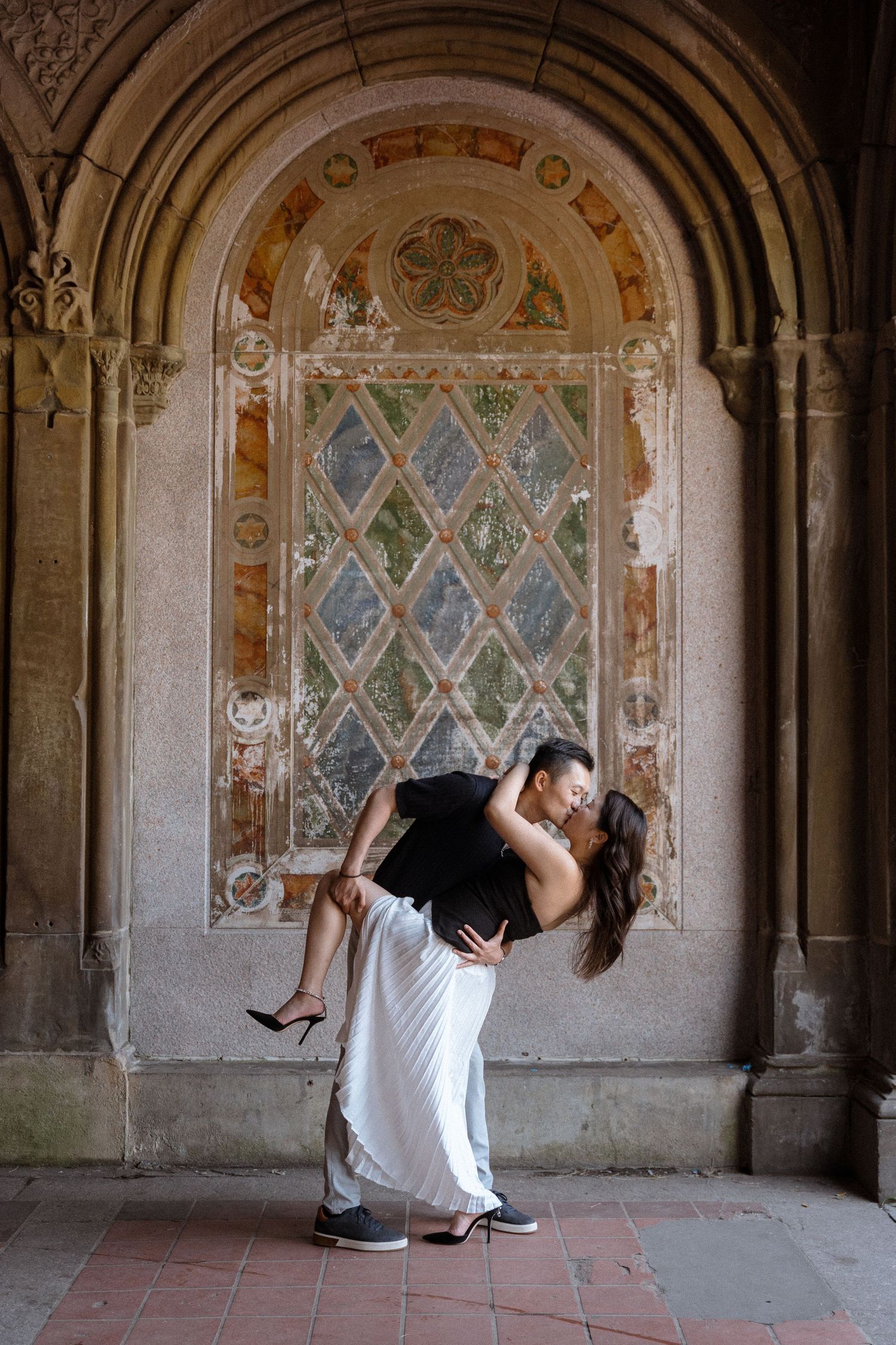 A couple dances beneath ornate stone archways with stained glass windows.