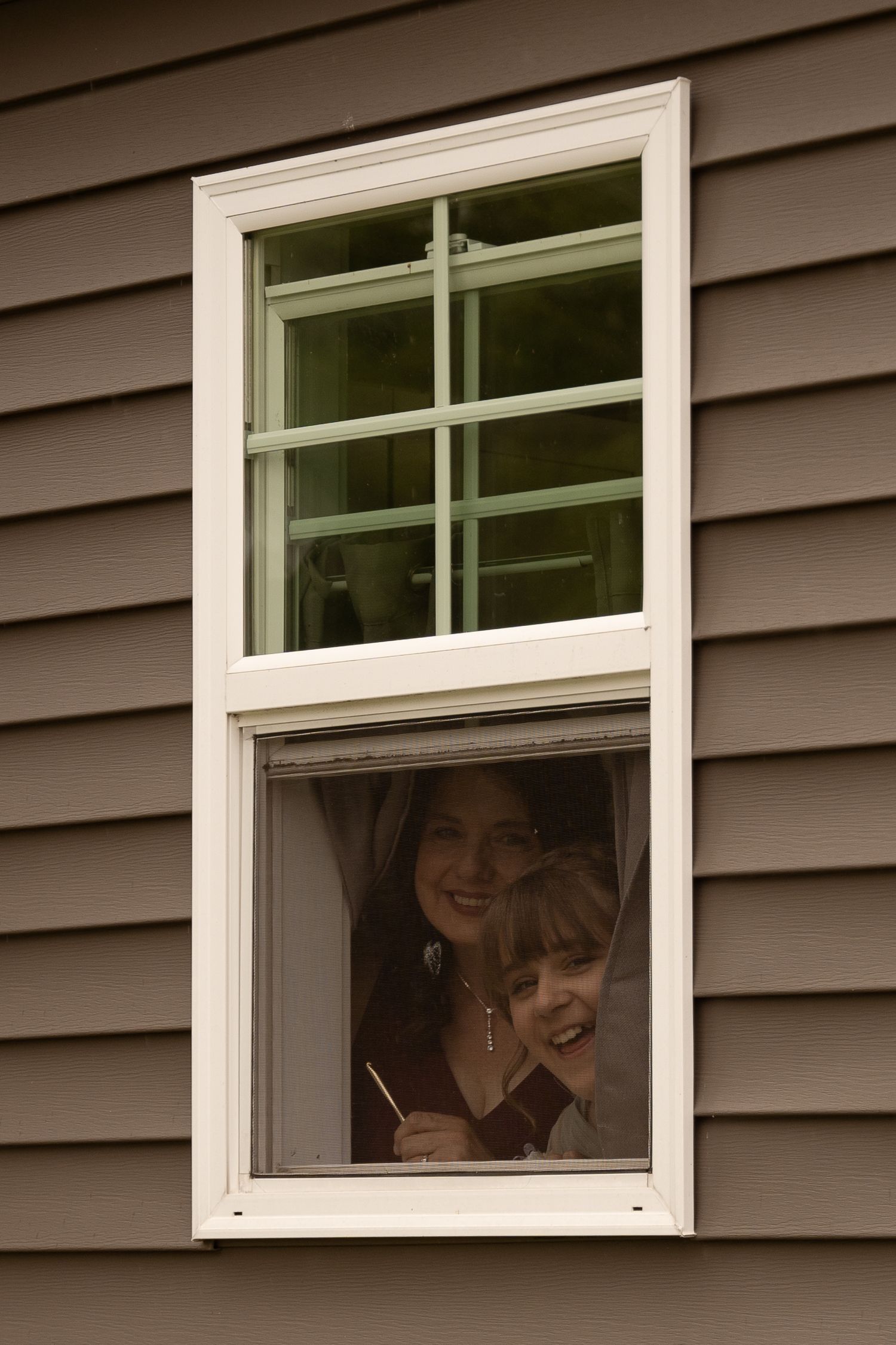 People smiling through white-framed windows of a grey-sided building.