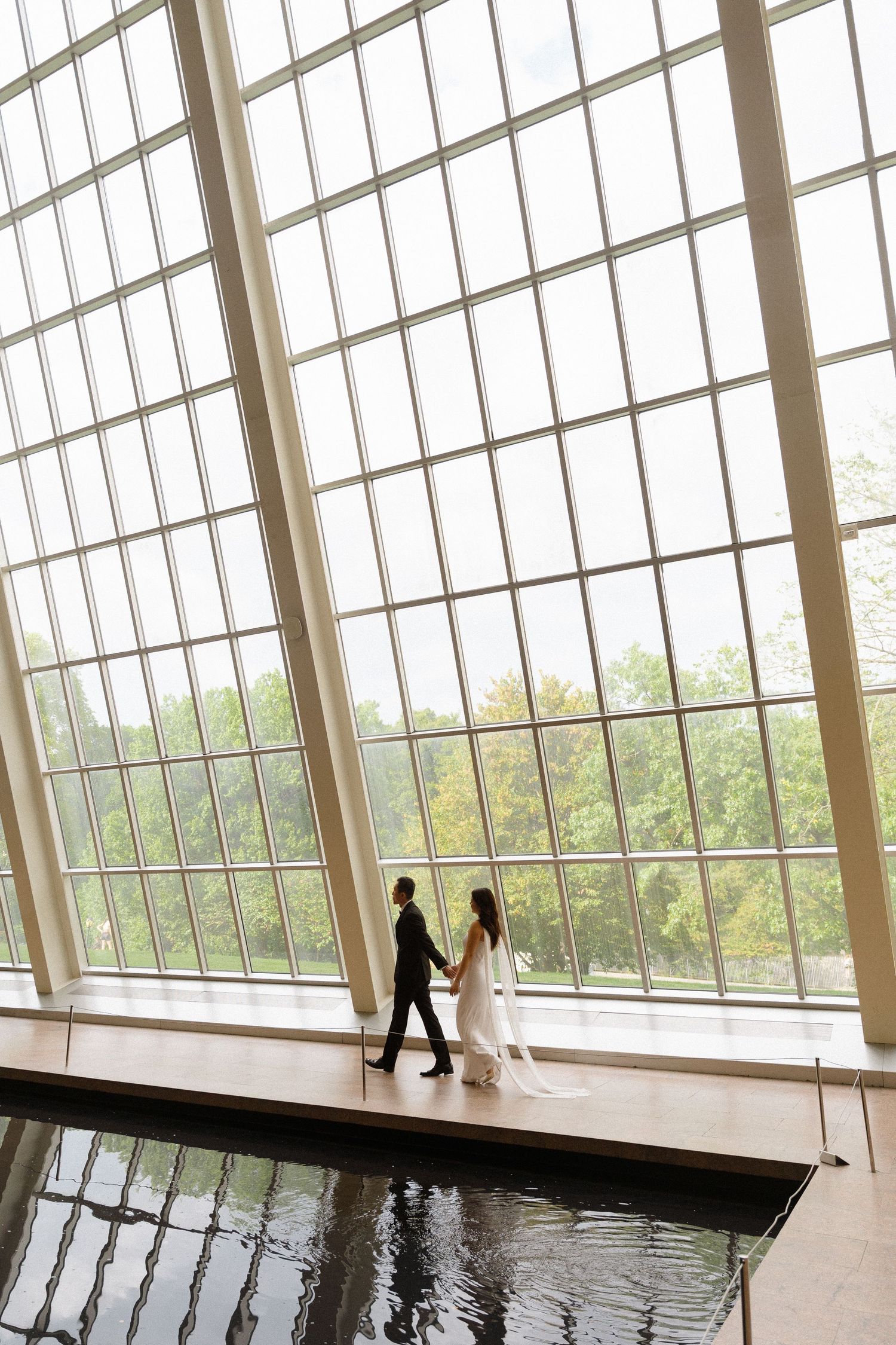 Two figures stand near dramatic slanted windows overlooking a scenic landscape.