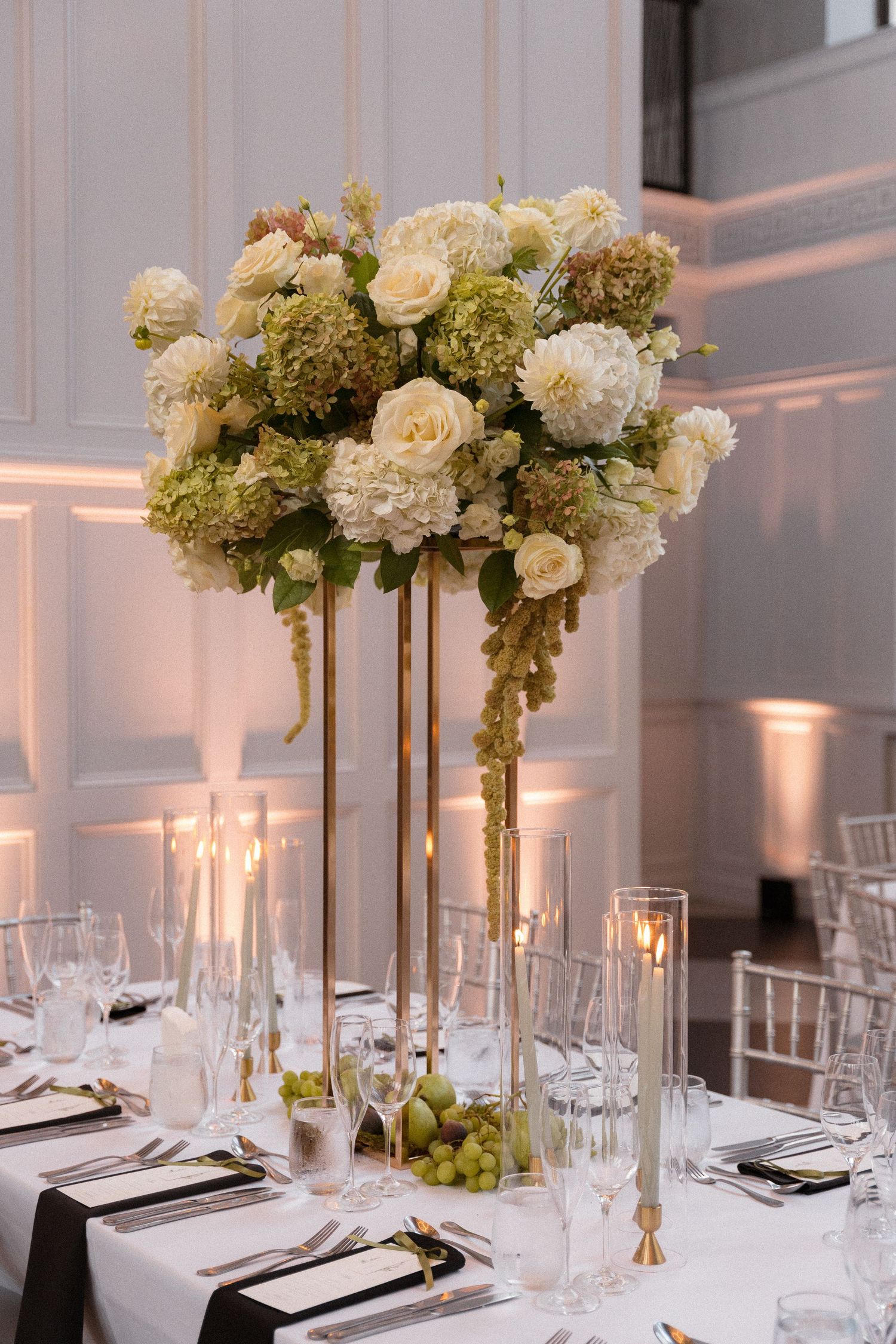 Elegant white floral centerpieces with tall gold stands decorate formal wedding reception tables.