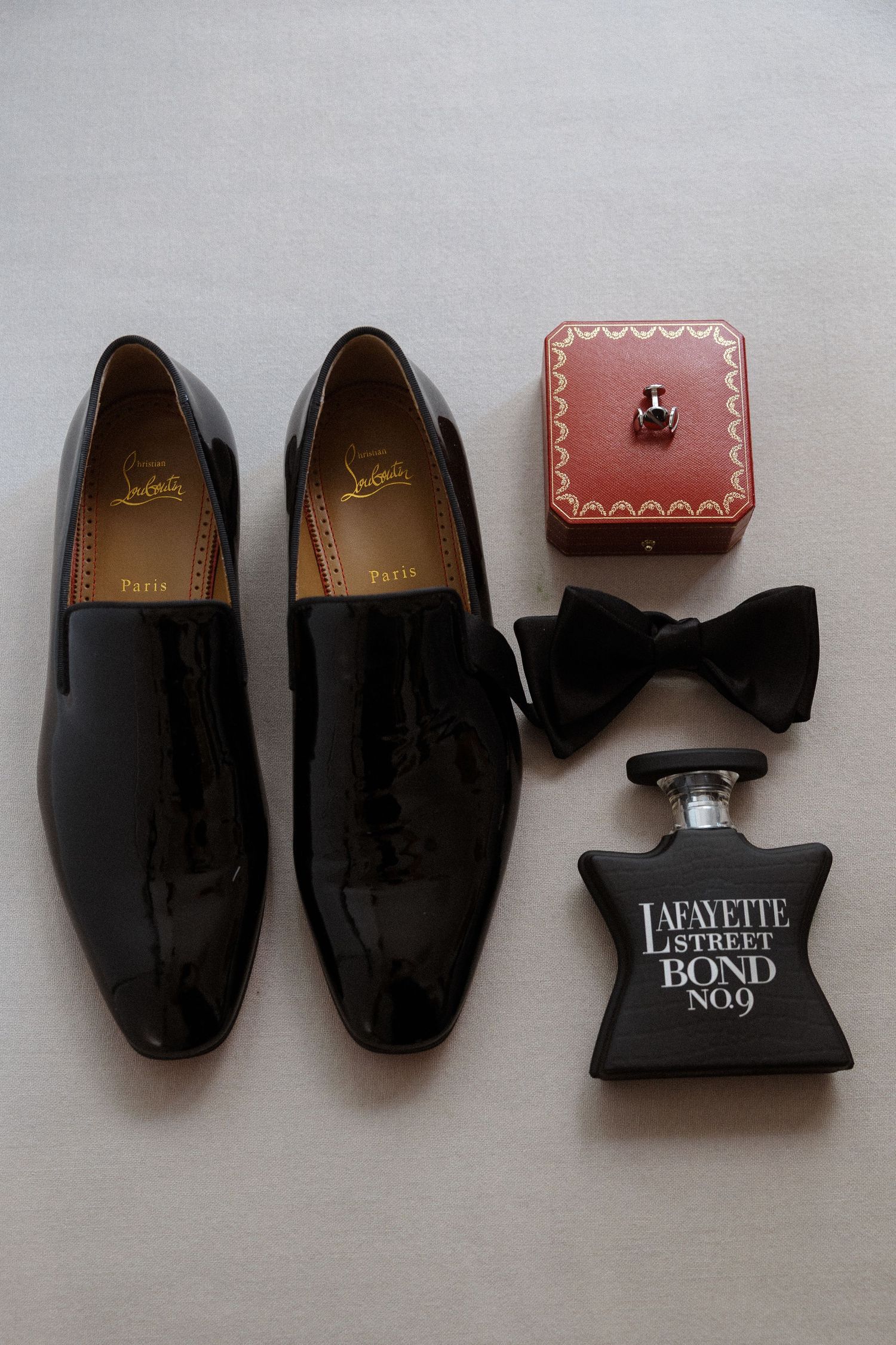 Black formal shoes and bow tie arranged with wedding accessories on gray background.