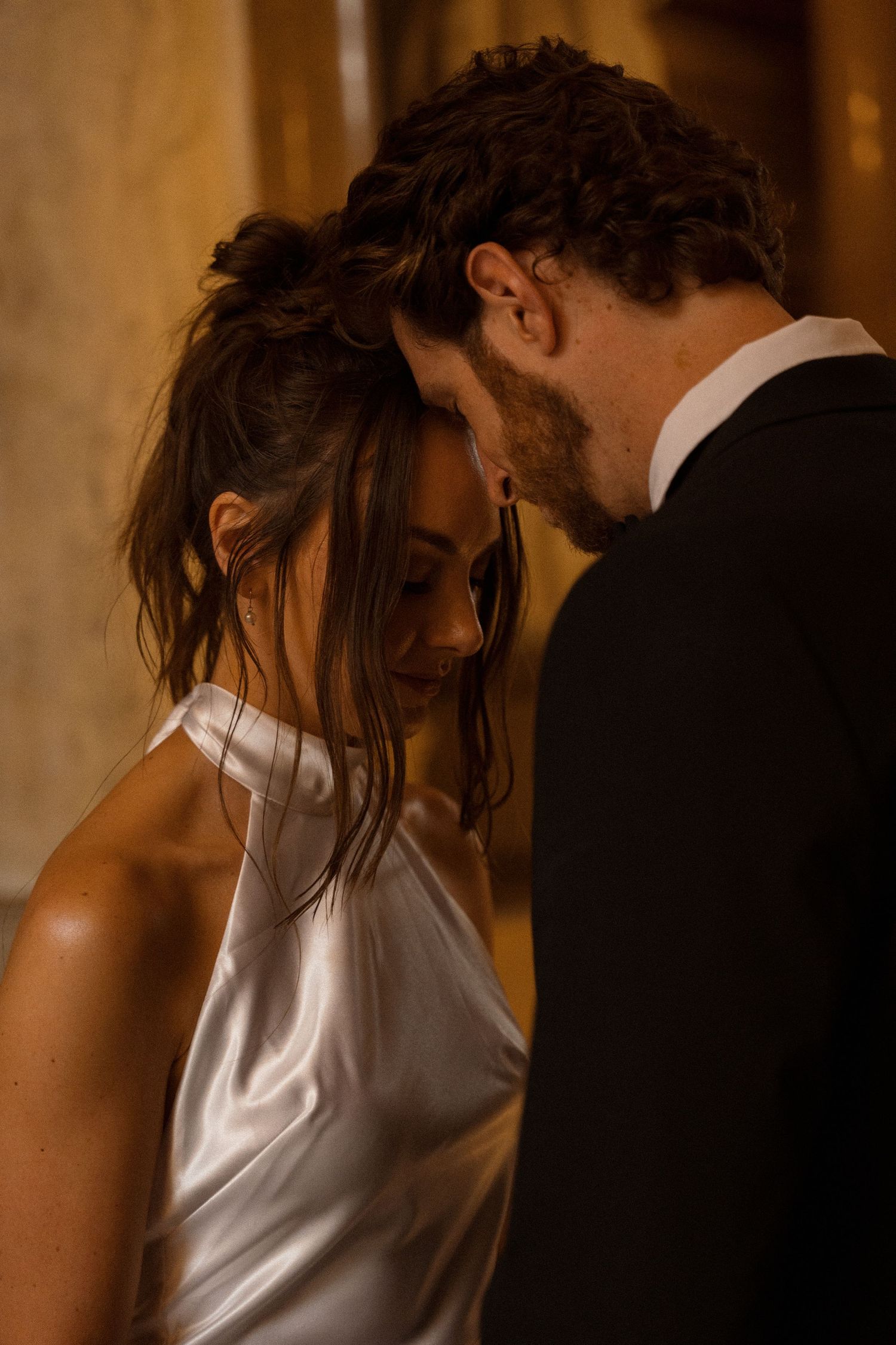 Intimate moment between a couple in formal attire in a warmly lit hallway.