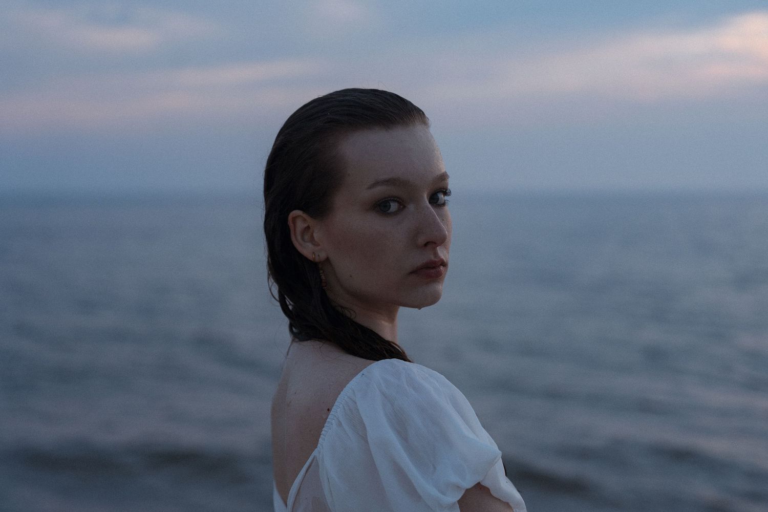 Woman in white dress against ocean backdrop during golden hour.