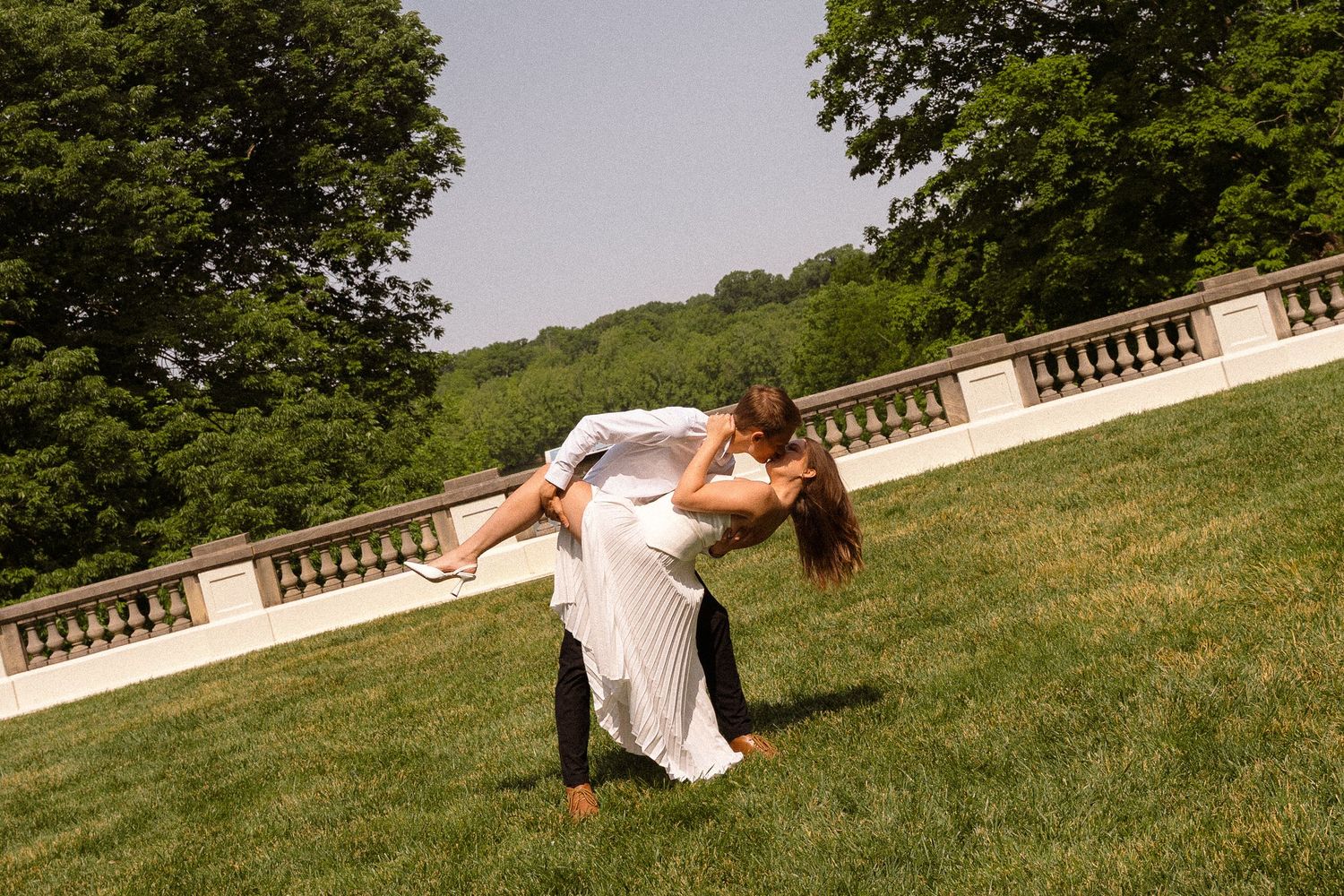 Playful wedding couple poses on a grassy hillside in a park setting.