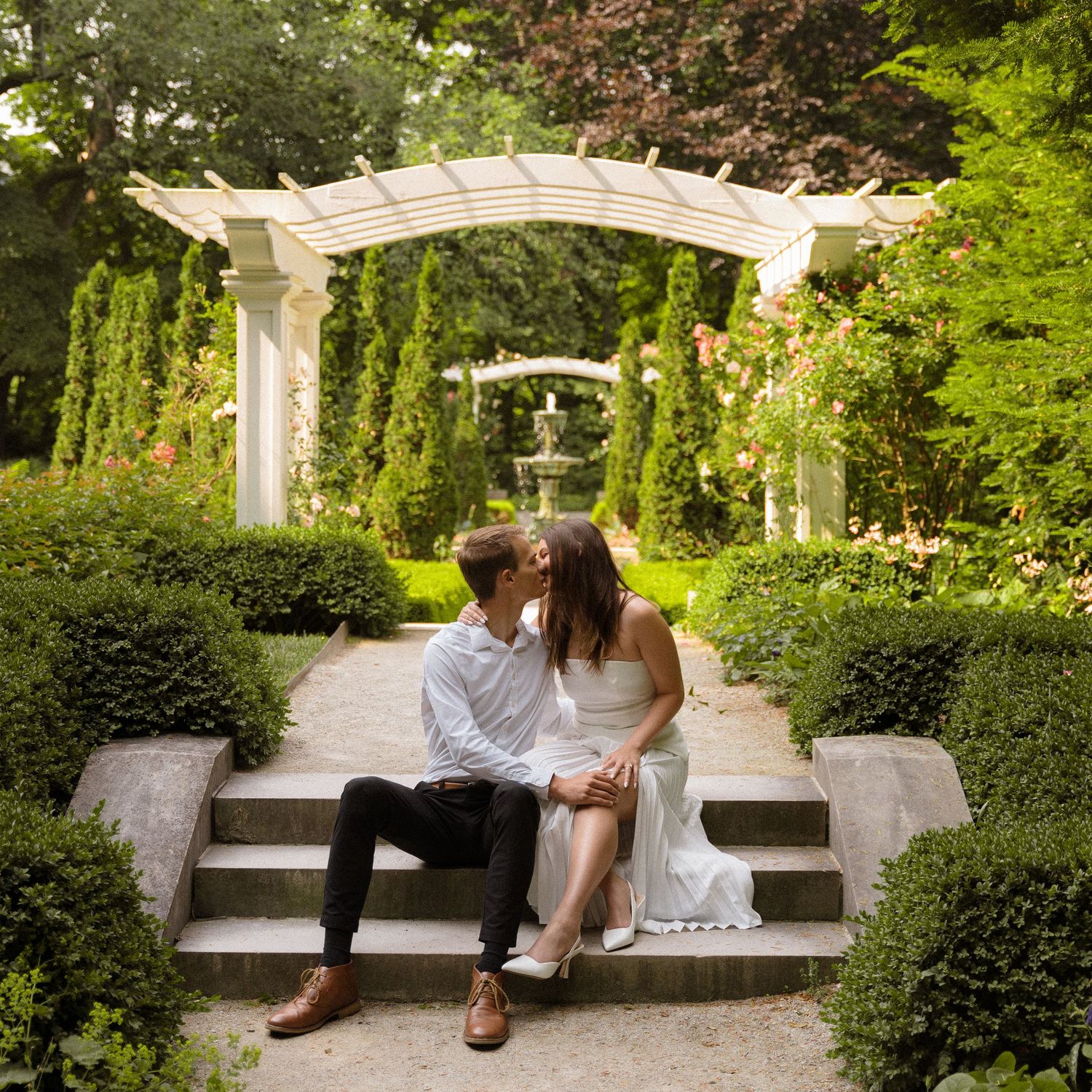 A romantic garden setting with white pergola, stone benches, and lush greenery.