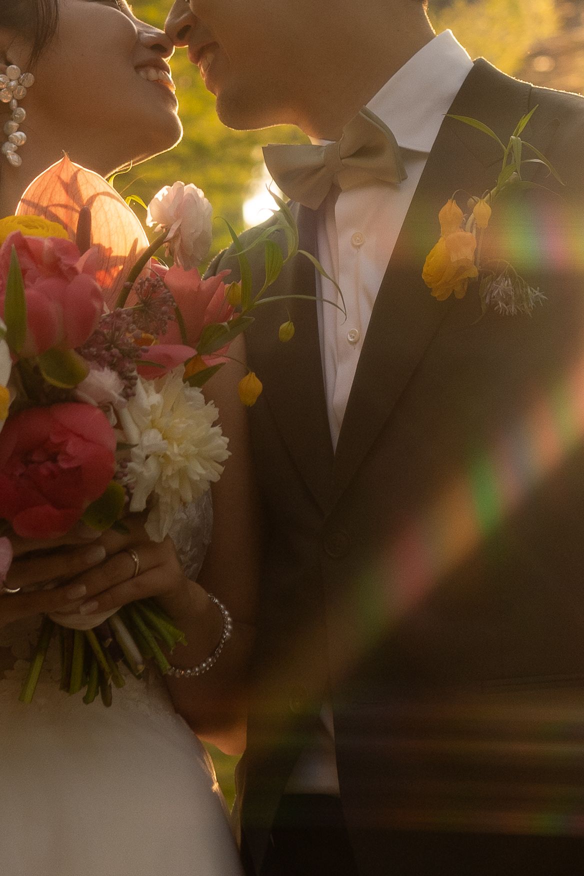 Wedding couple silhouetted against golden sunset light with colorful floral bouquet details.