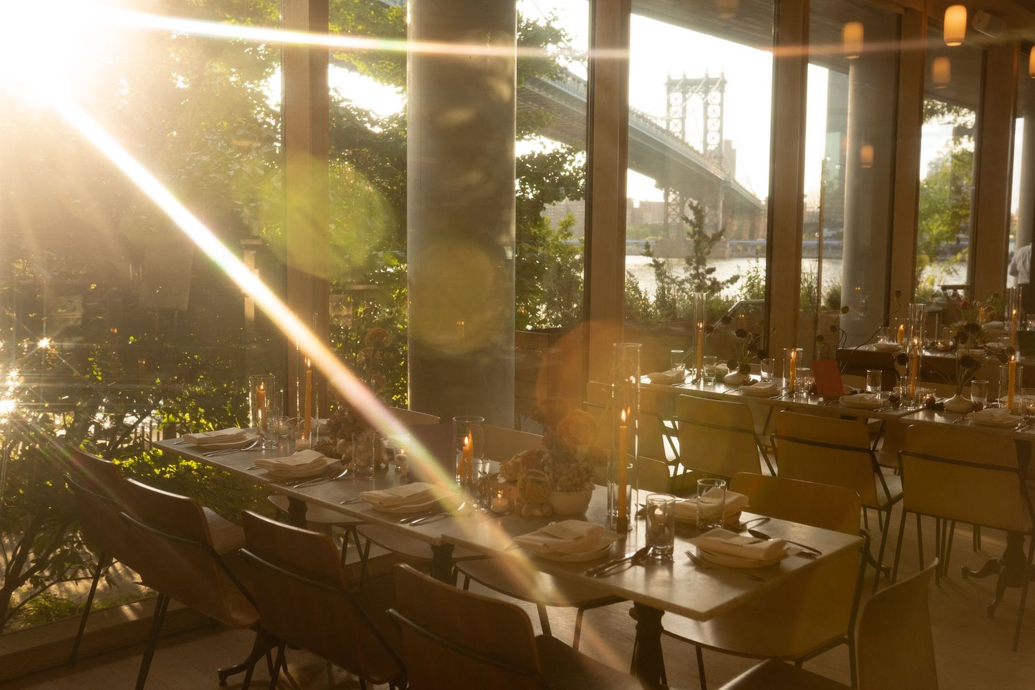 Warm sunlight streams through windows in an elegant dining space with wooden beams.