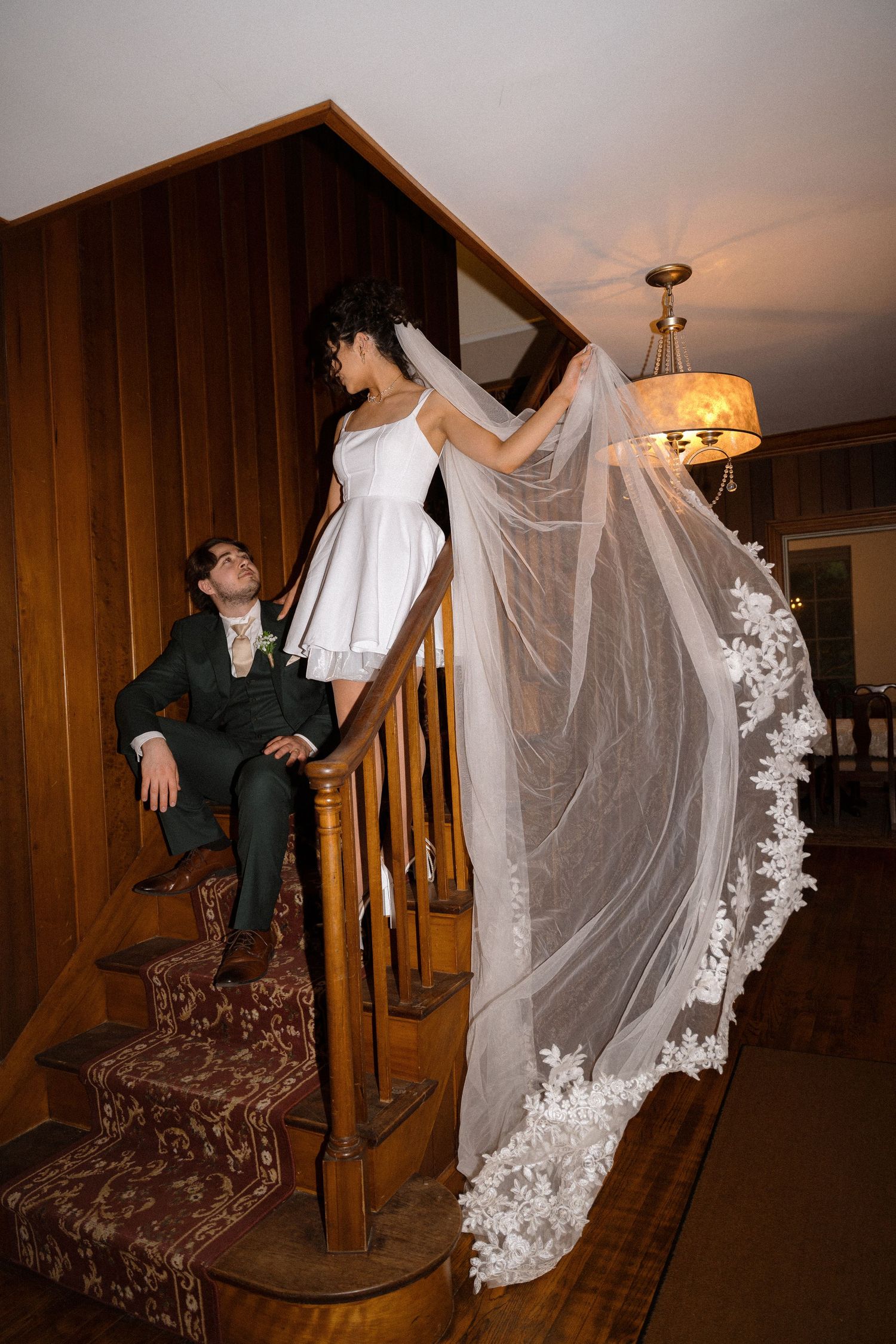 Wedding couple creates fun photo series on wooden staircase with flowing veil.