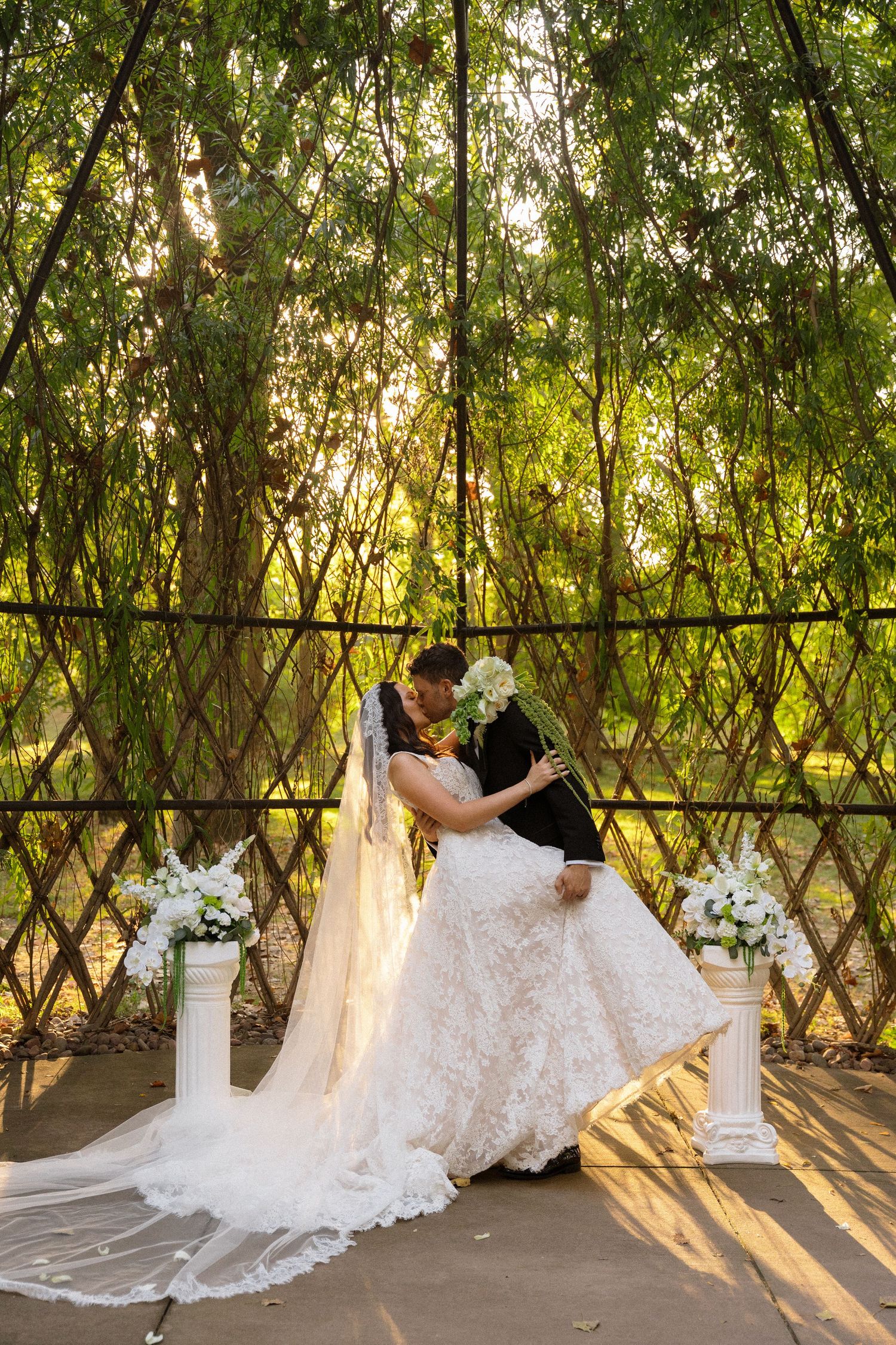 Elegant wedding scene with flowing dress and floral arrangements under a natural green canopy.