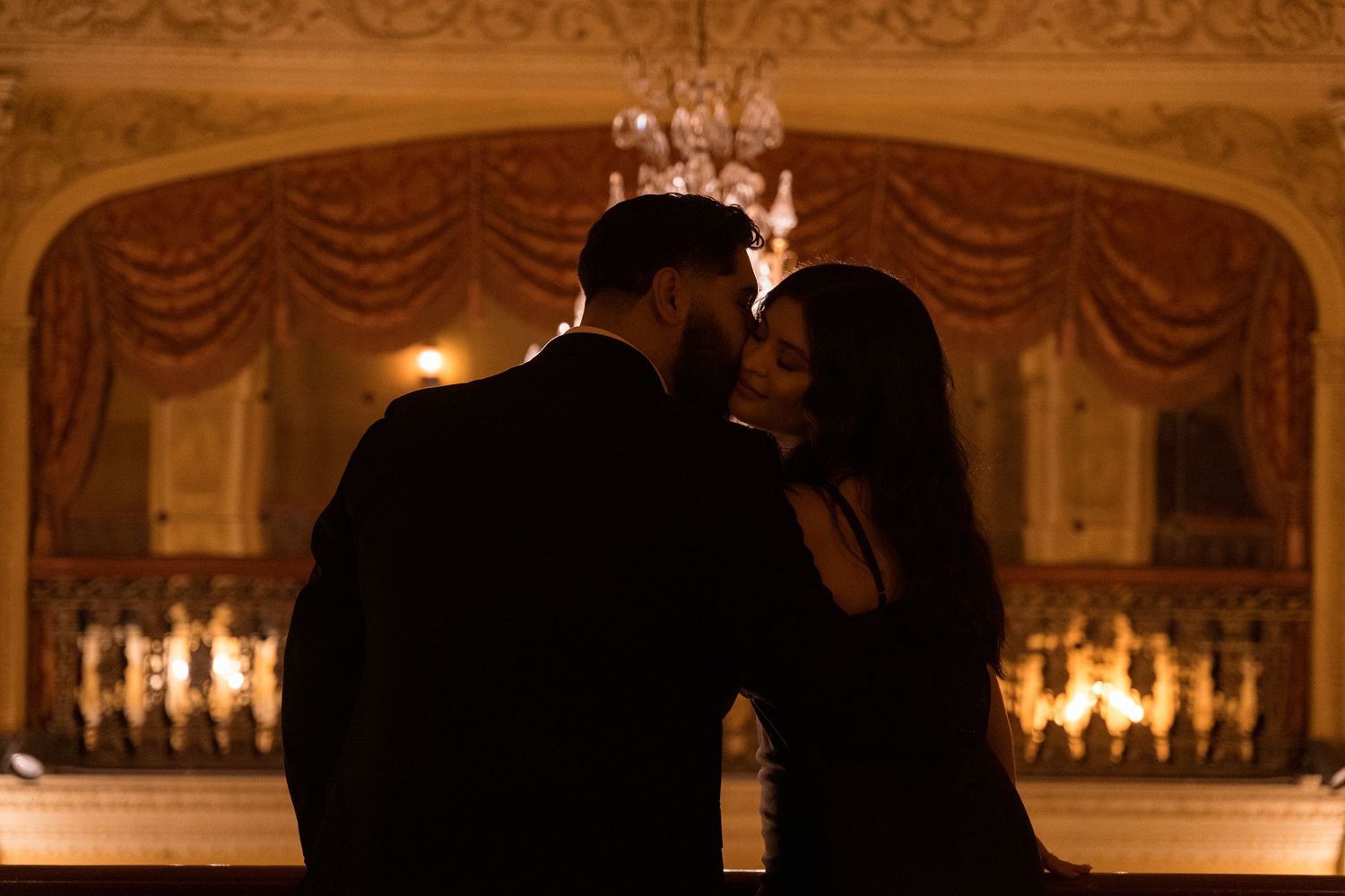 A grand ballroom with ornate architecture and crystal chandeliers lit in warm amber tones.