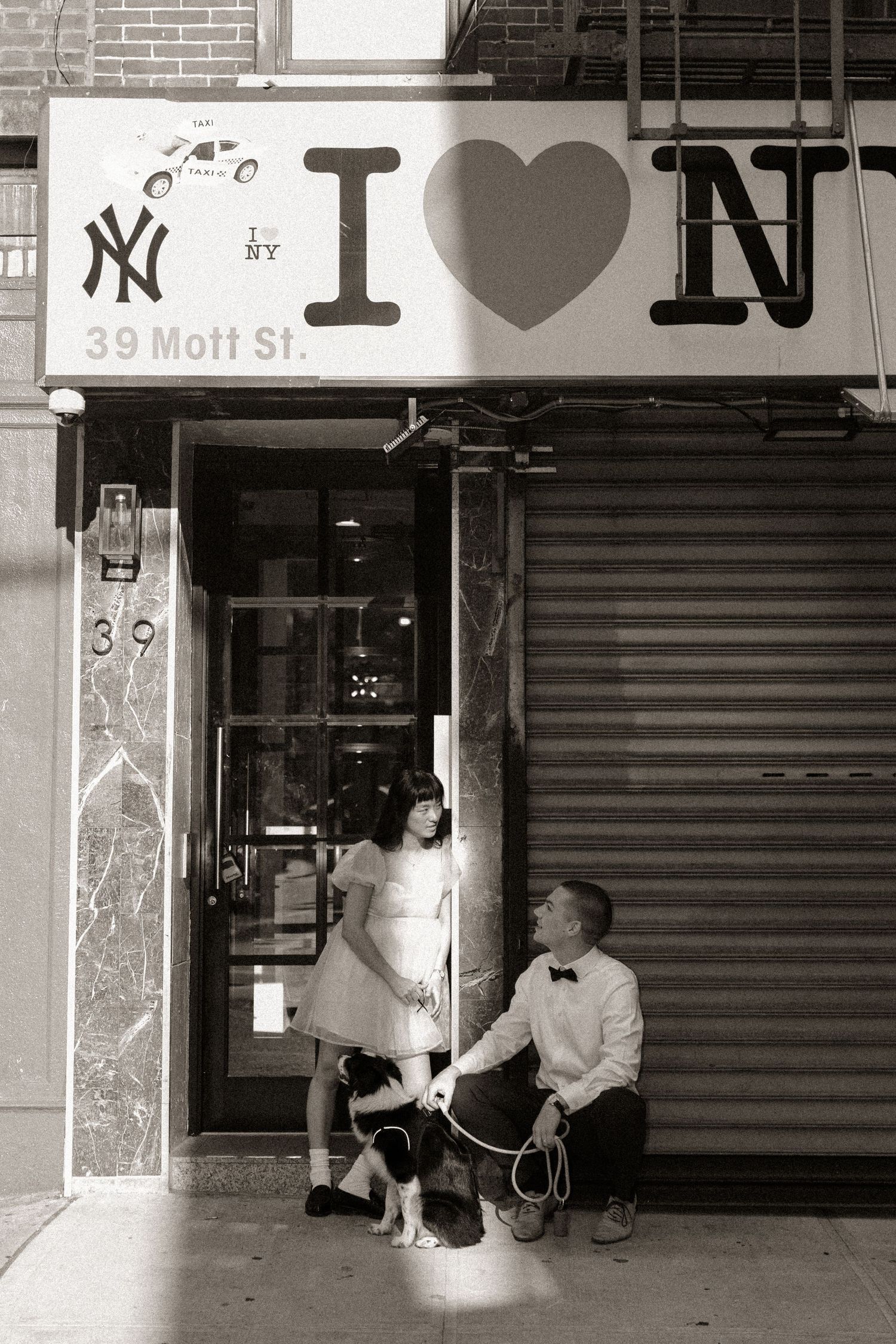 Black and white urban street scene showing storefronts with I heart NY signage.