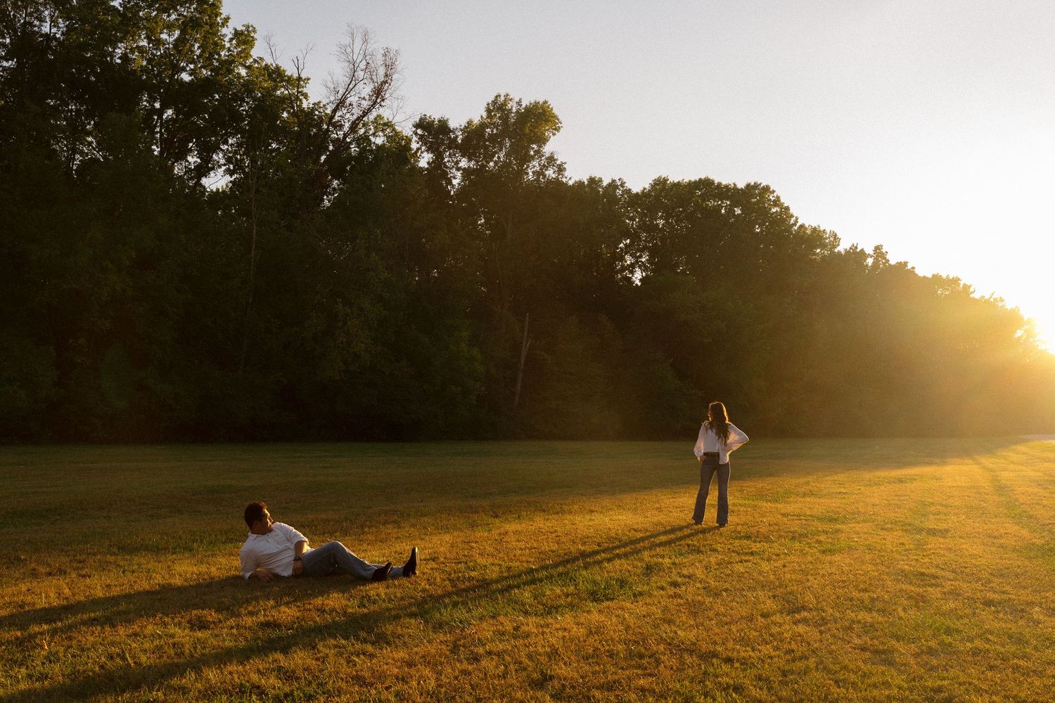 Two people enjoying a sunset in a grassy field with trees.