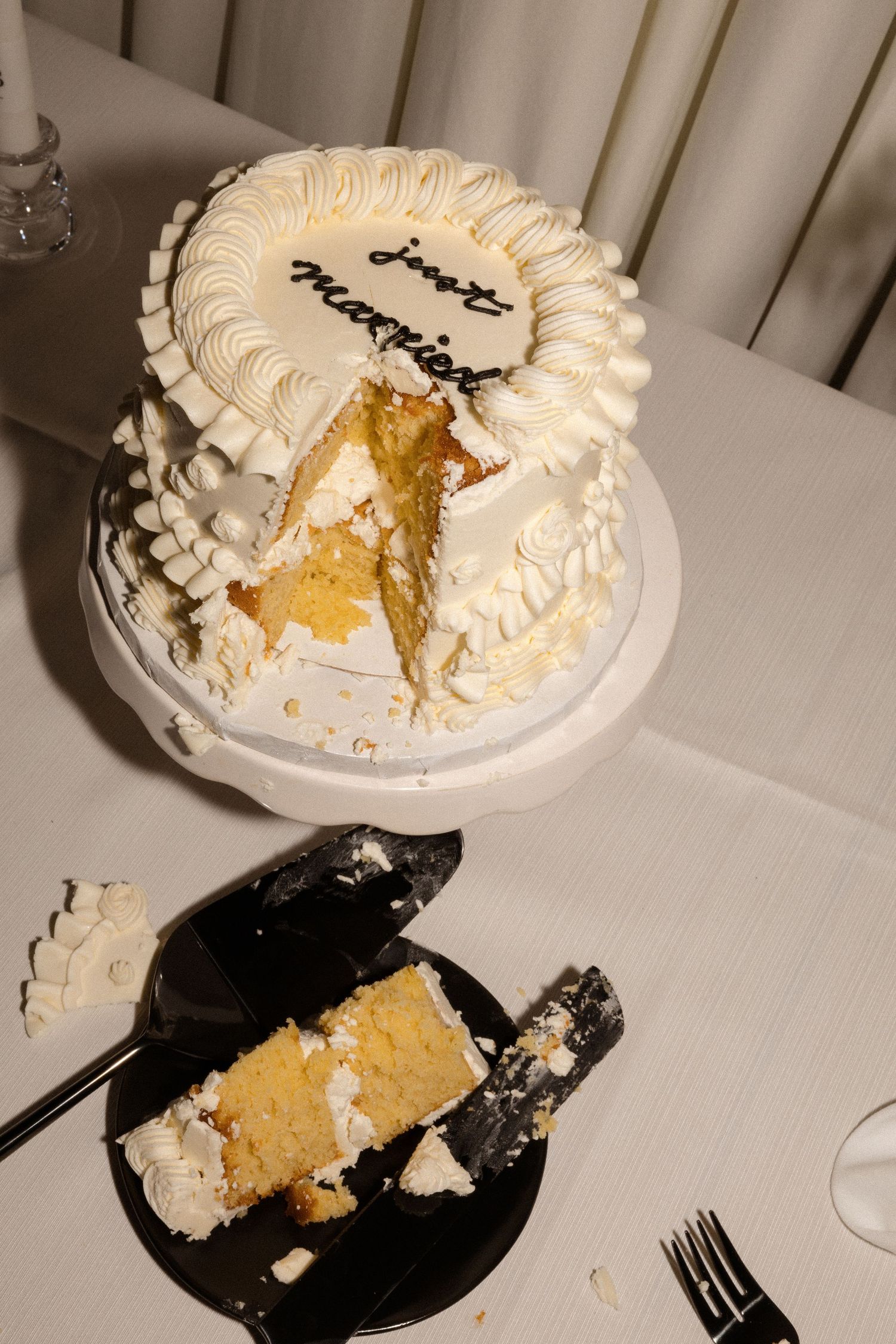 A partially eaten white wedding cake with pieces served on black plates.