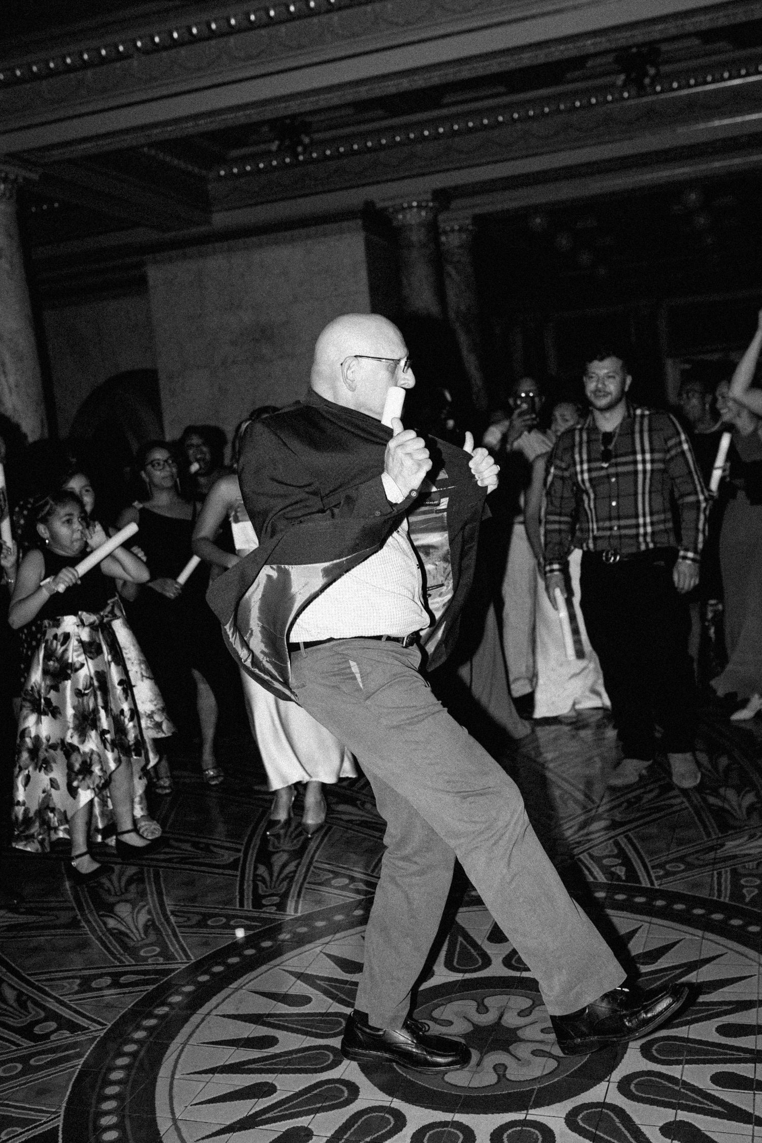 Black and white photo of people dancing energetically on a patterned ballroom floor.