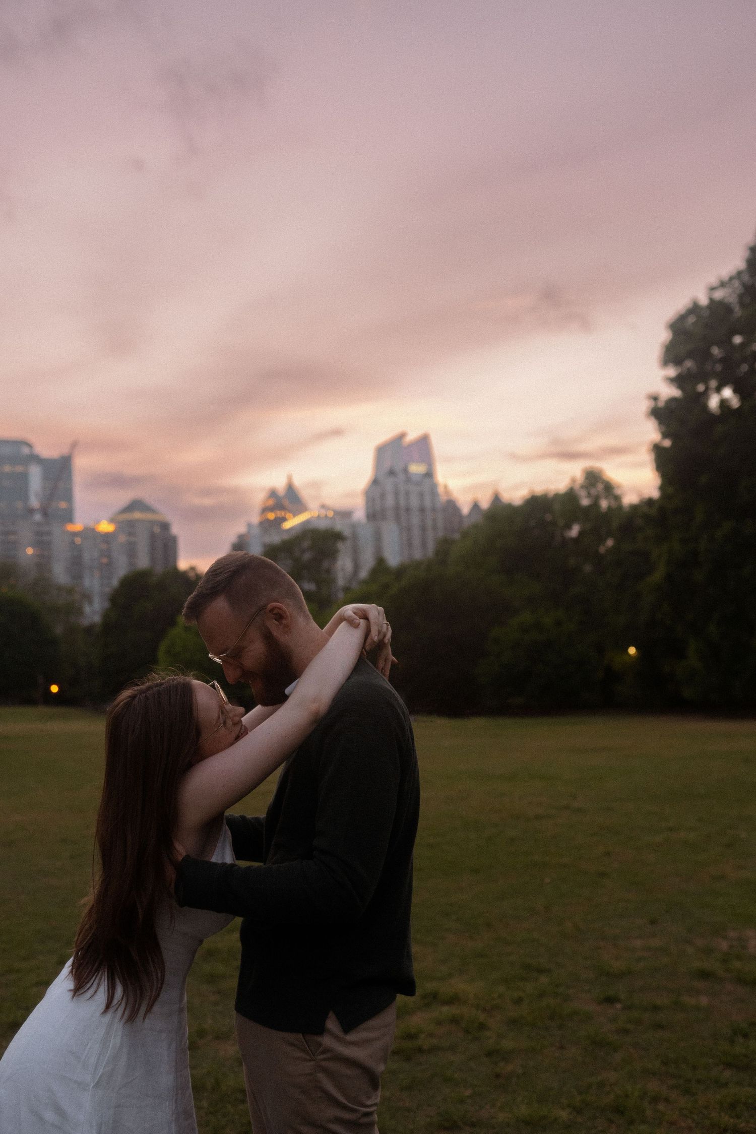 Romantic sunset embrace in a city park with skyline backdrop.