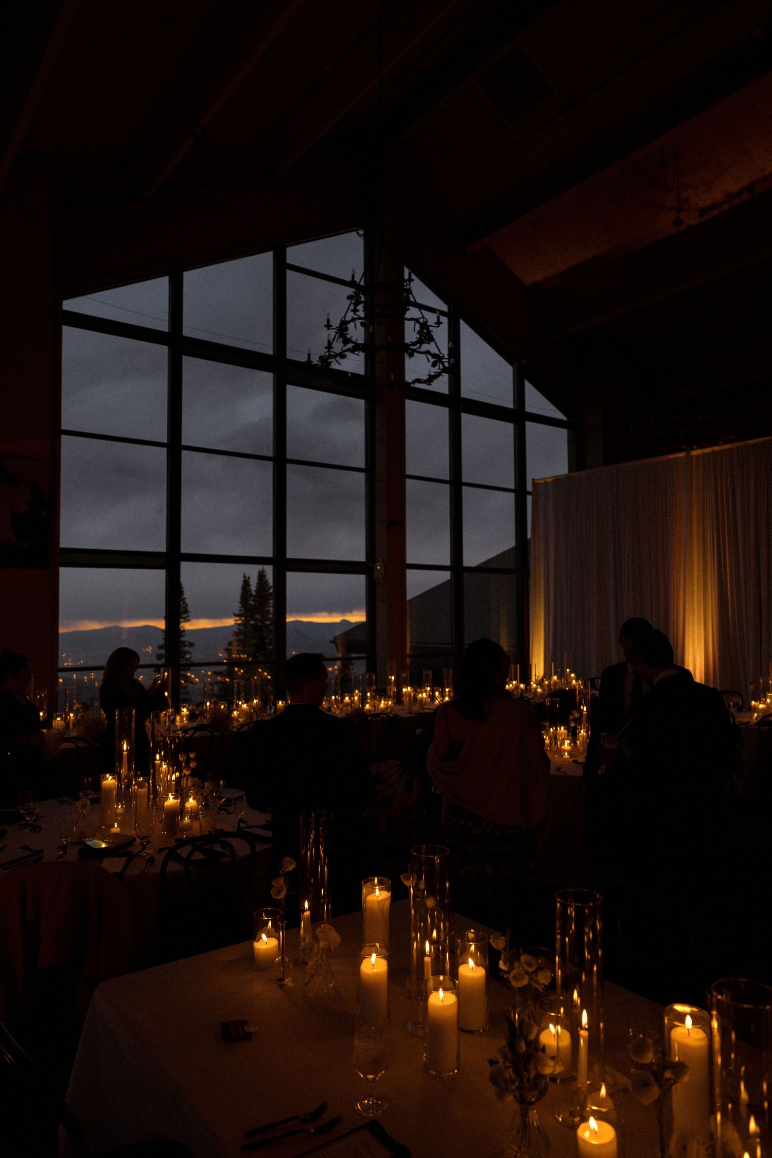Romantic candlelit reception venue with mountain views through large windows at dusk.