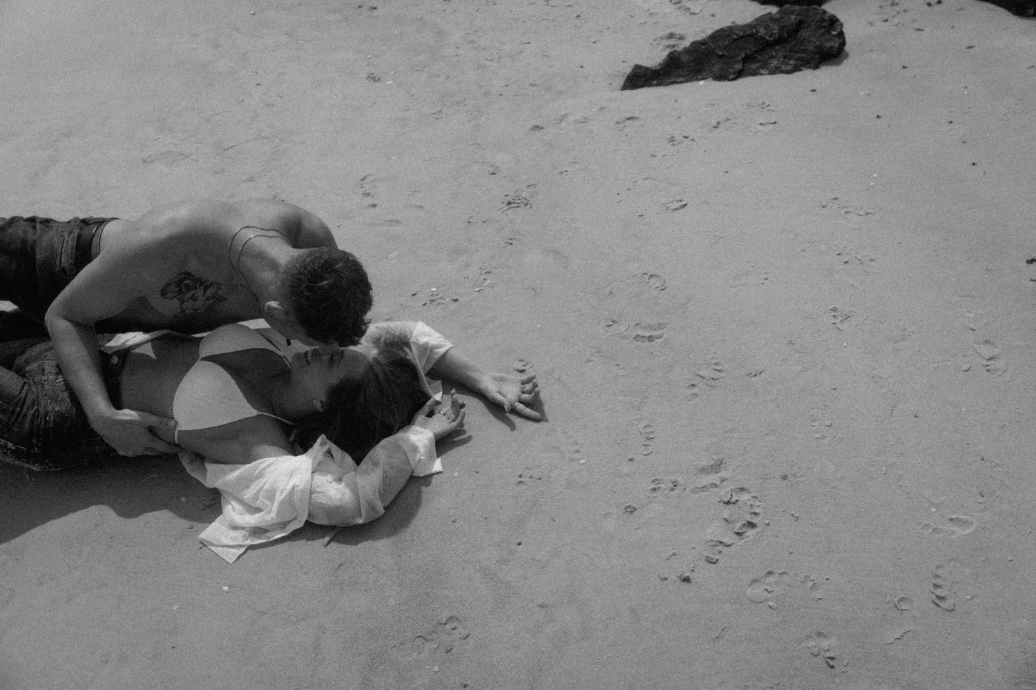 Black and white photo of couple lying on sandy beach.