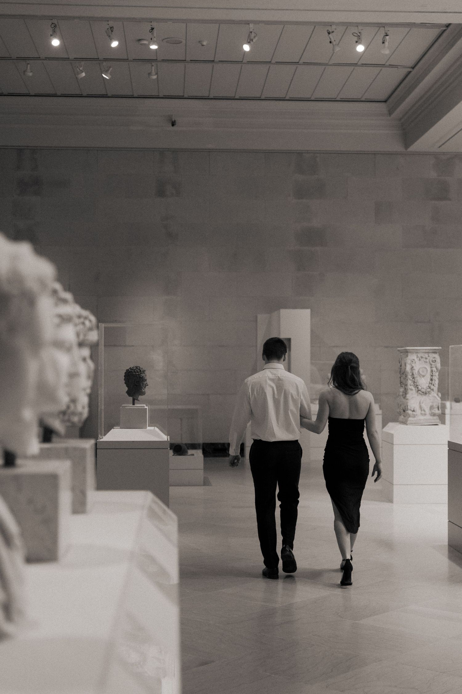 Silhouettes of people walking through a minimalist white gallery space.