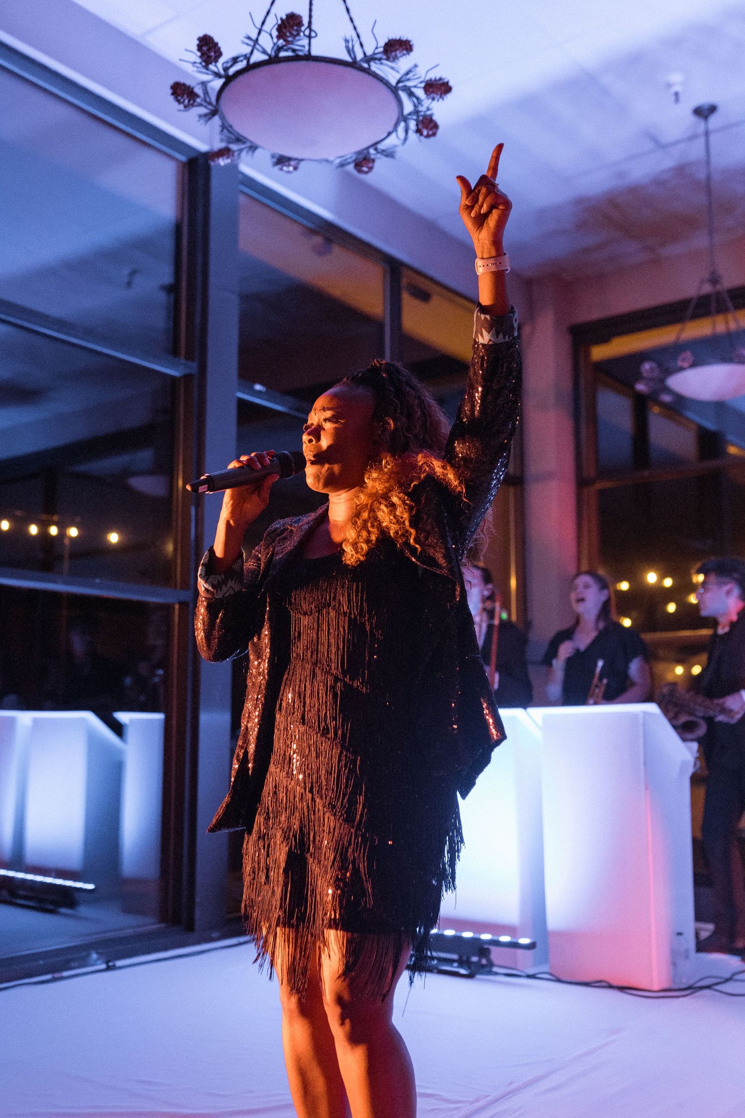Performer in black fringe dress singing on stage with dramatic lighting.