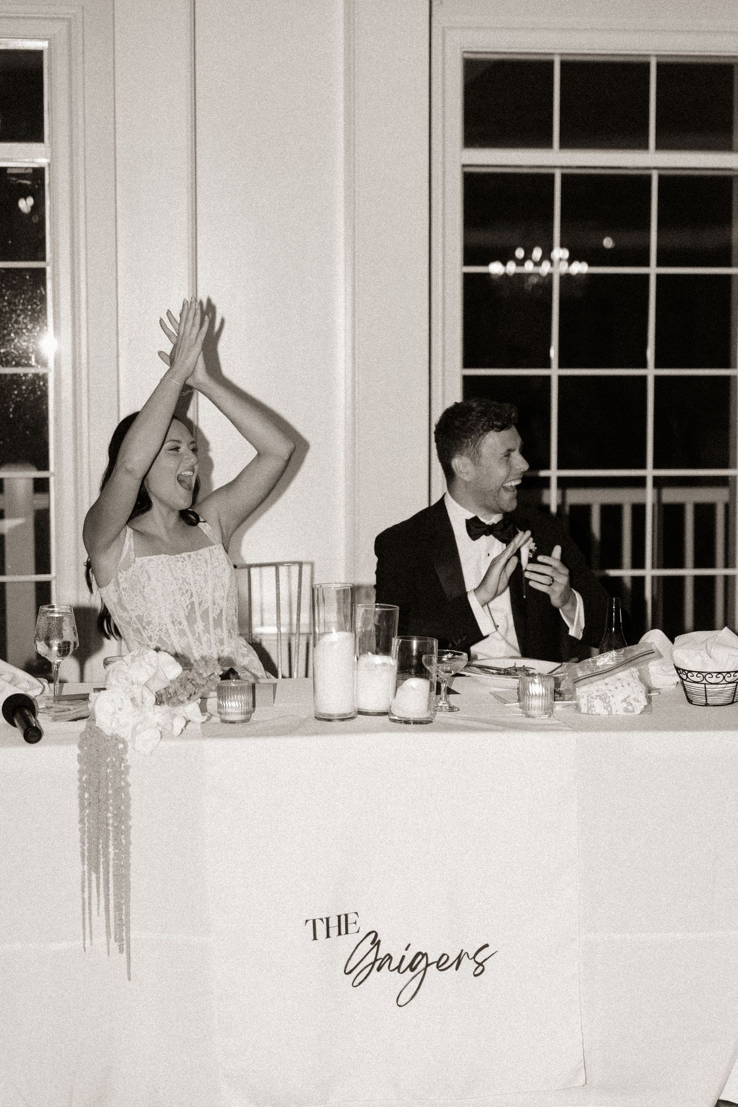 Wedding reception guests celebrate at a formal dinner table with raised hands and joyful expressions.