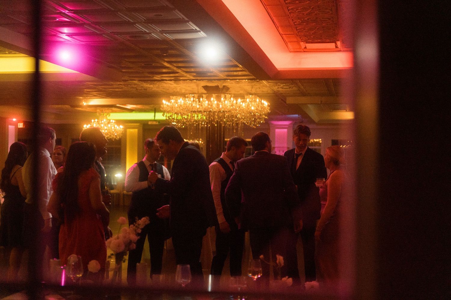 A dimly lit reception venue with colorful ambient lighting and silhouettes of guests.