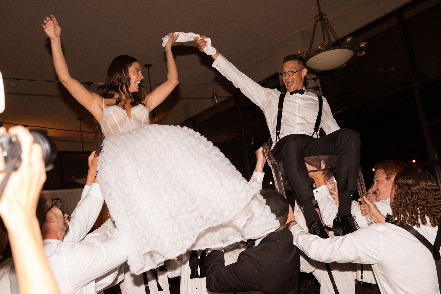 Wedding guests dancing with arms raised on a dark dance floor.