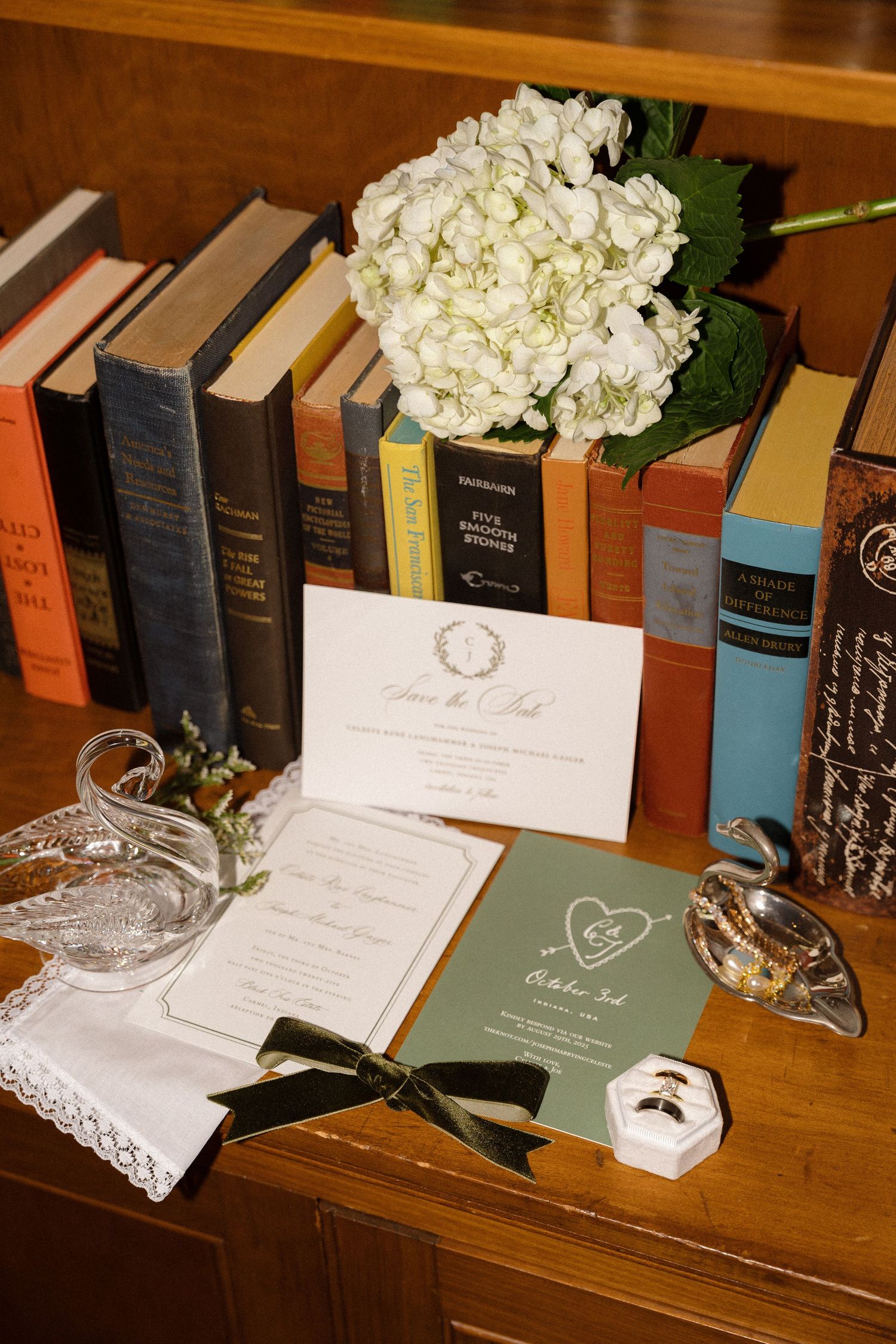 Wedding stationery display with hydrangeas and vintage books on wooden surface.