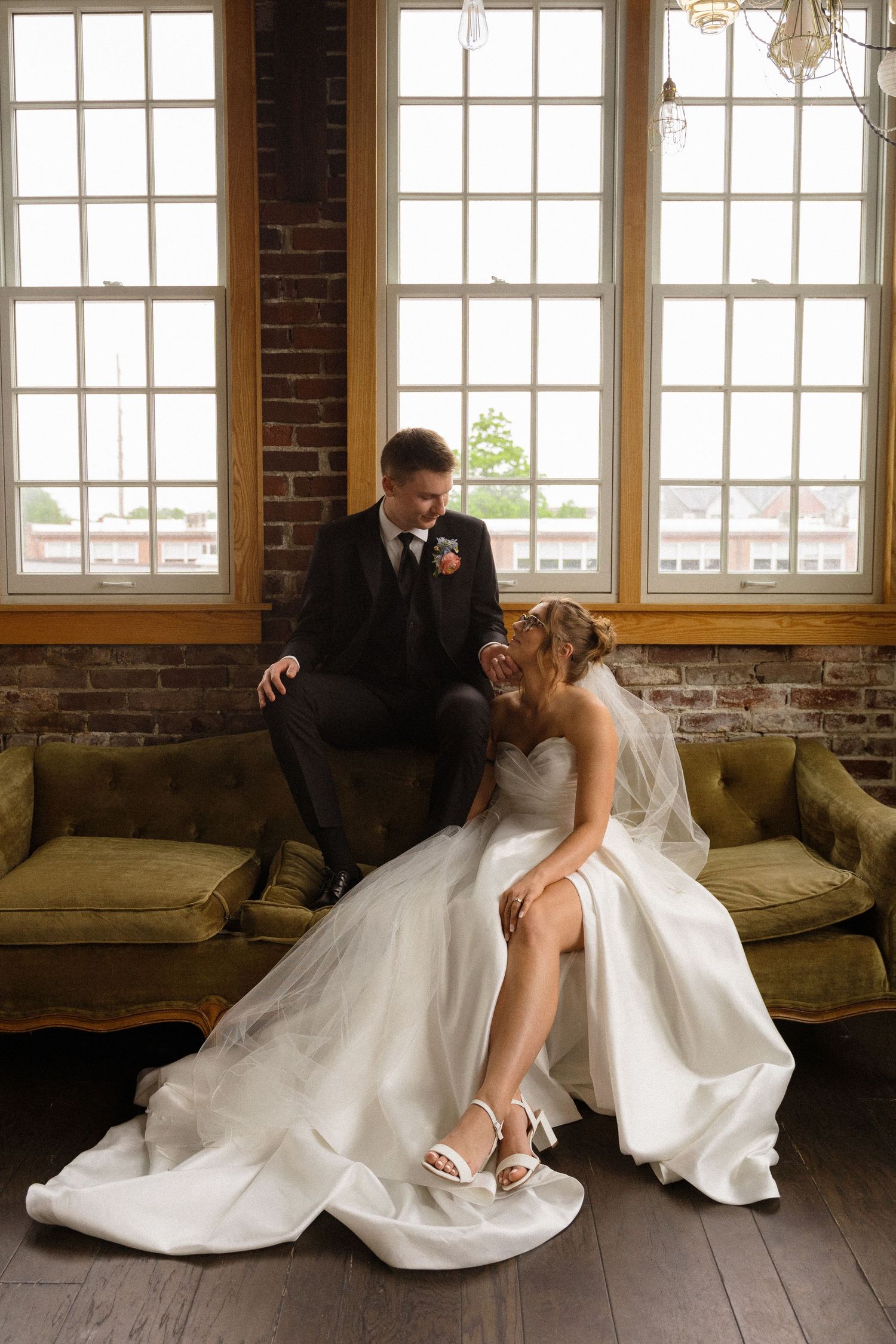 Wedding couple posing playfully on vintage couch in industrial brick loft space.