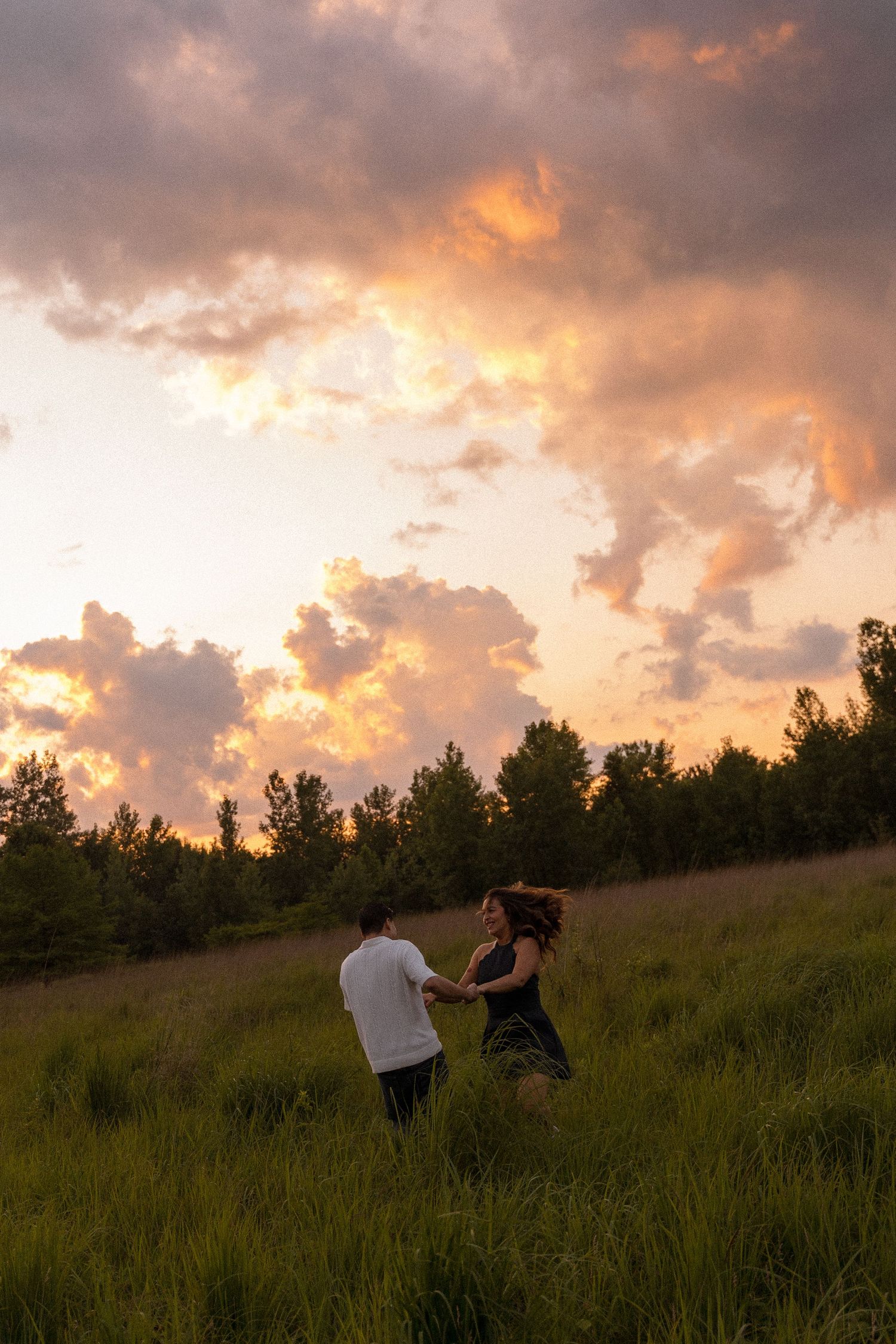 Couple walking through a meadow under a vibrant sunset sky.