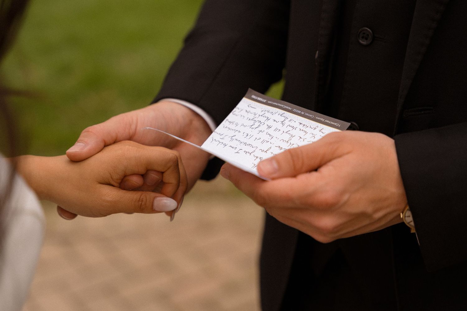 Close-up of hands exchanging wedding vows on paper during ceremony.