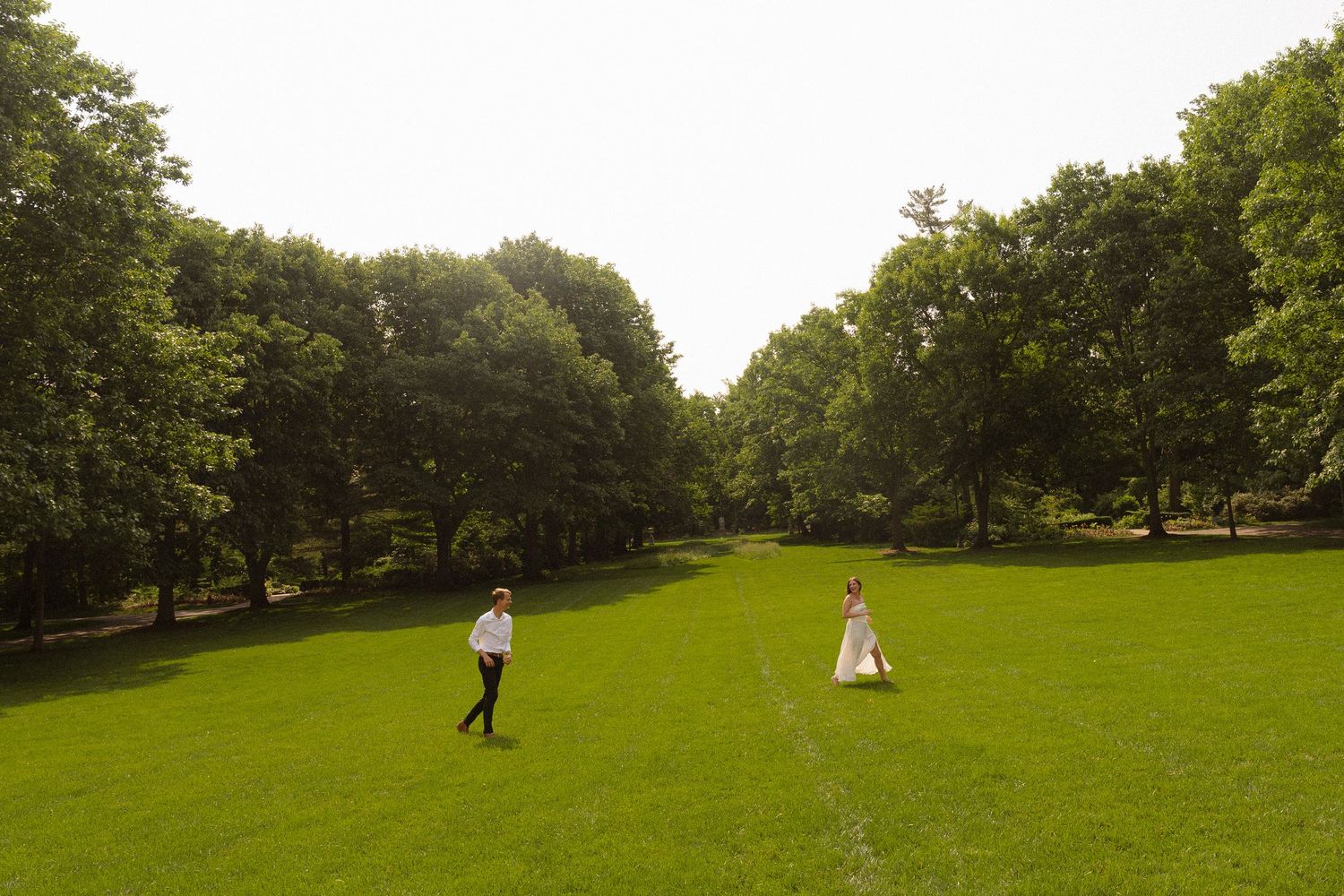 A panoramic view of a lush green park with distant figures on a sunny day.