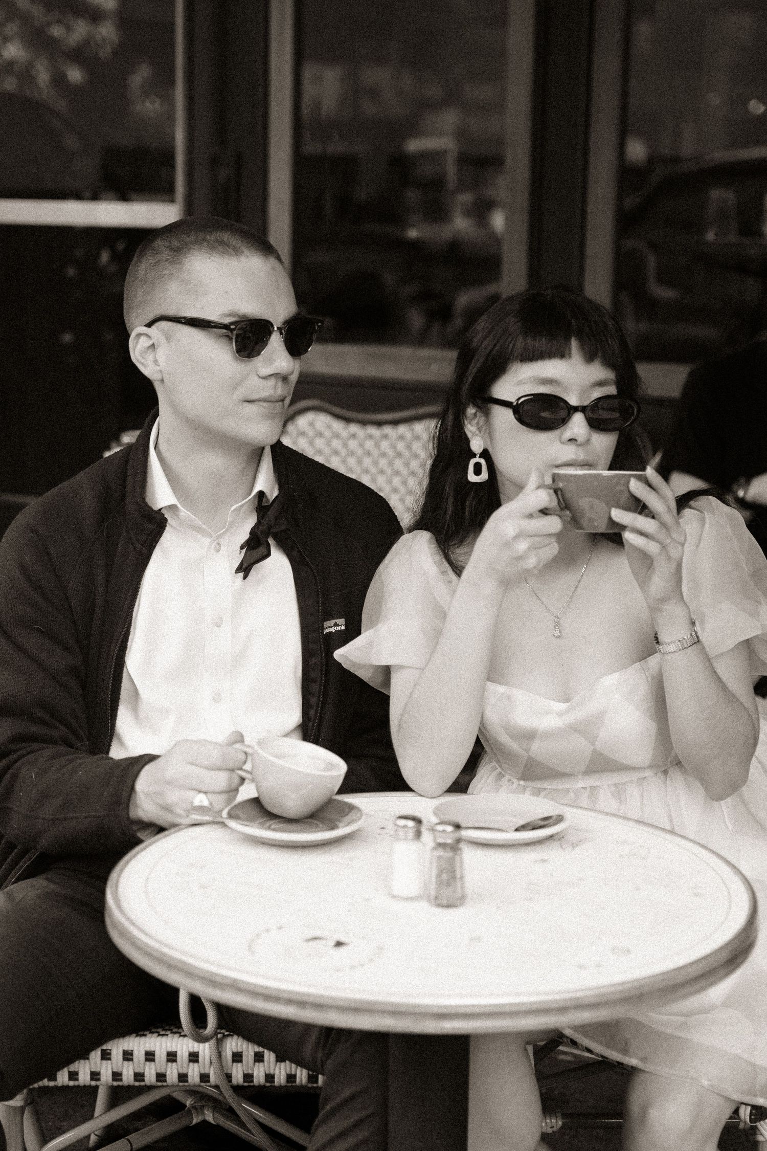 A couple seated at a white cafe table in vintage-style black and white photography.