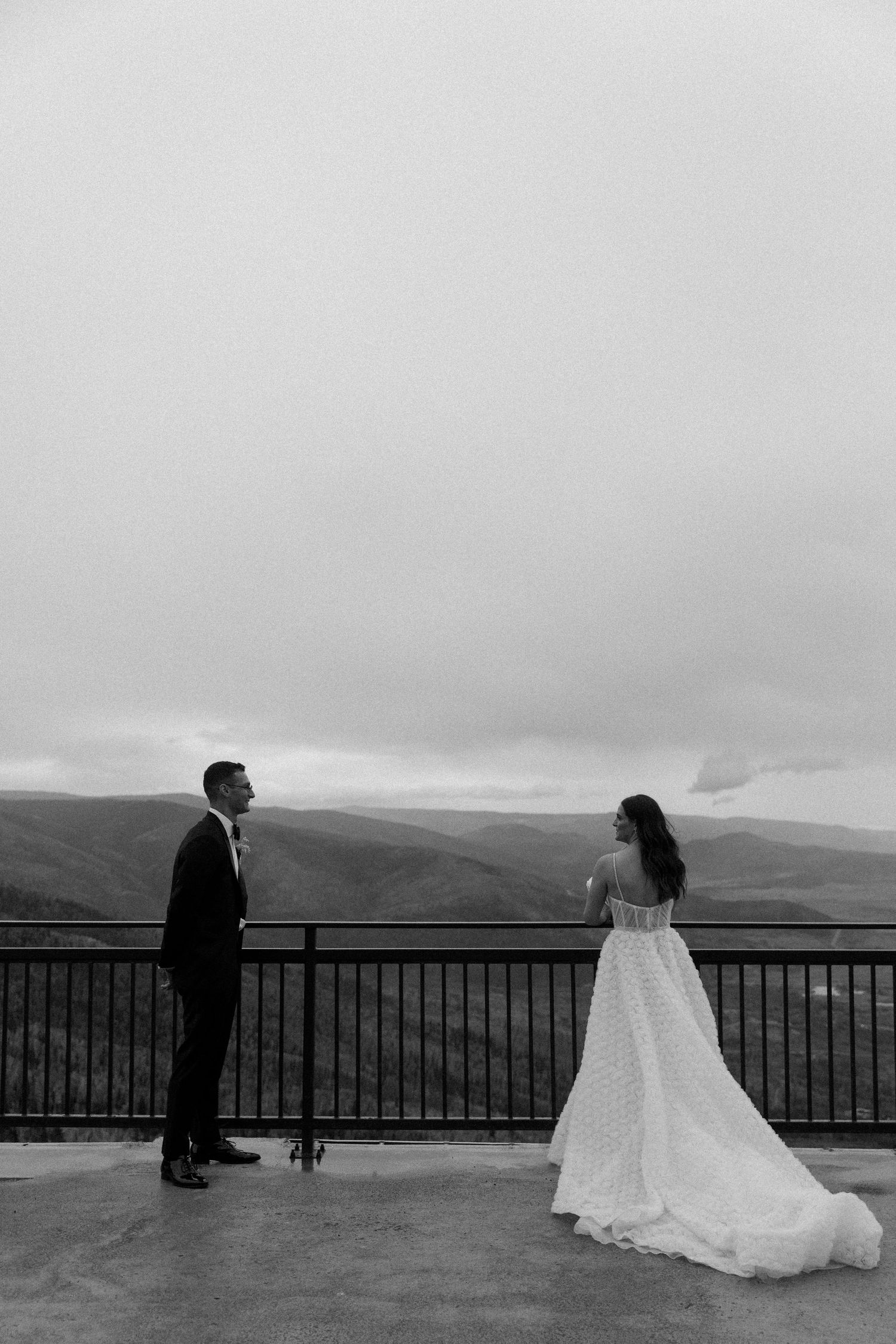 Wedding couple standing on a scenic overlook with mountain views.
