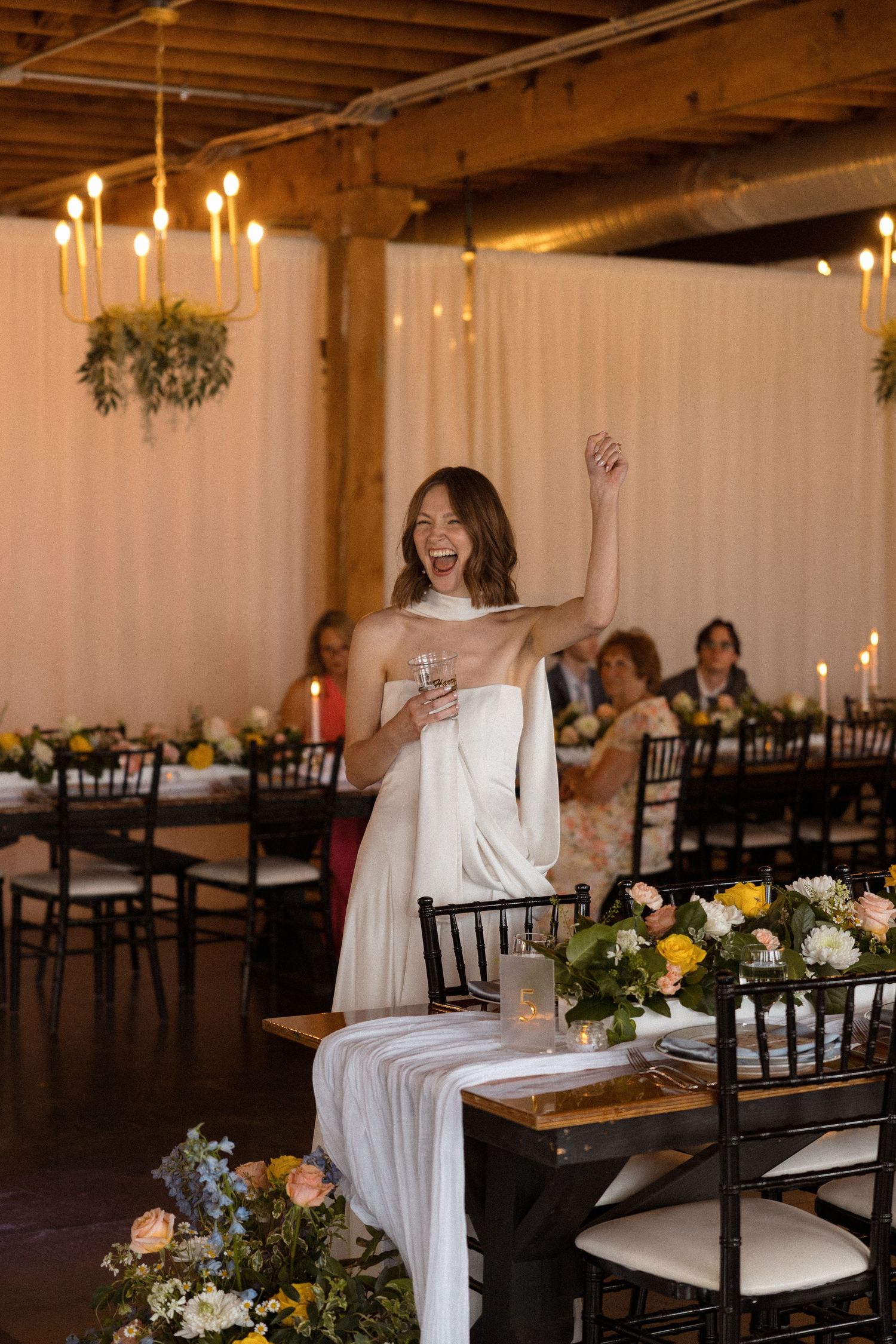 Reception venue with elegant table settings, white draping, and floral centerpieces.