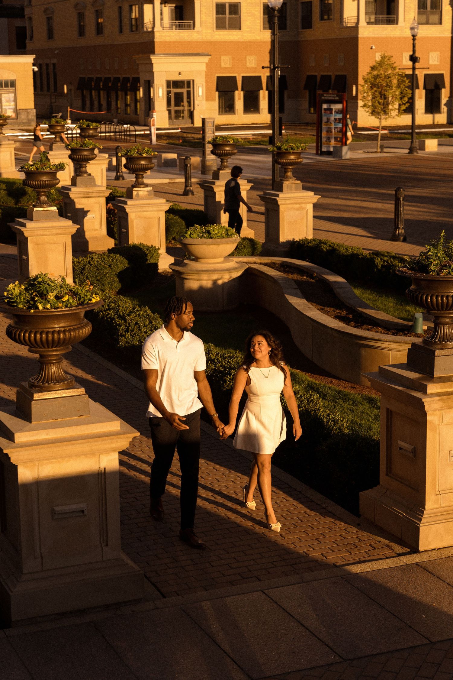 Two people walk along a colonnade at sunset casting long shadows.
