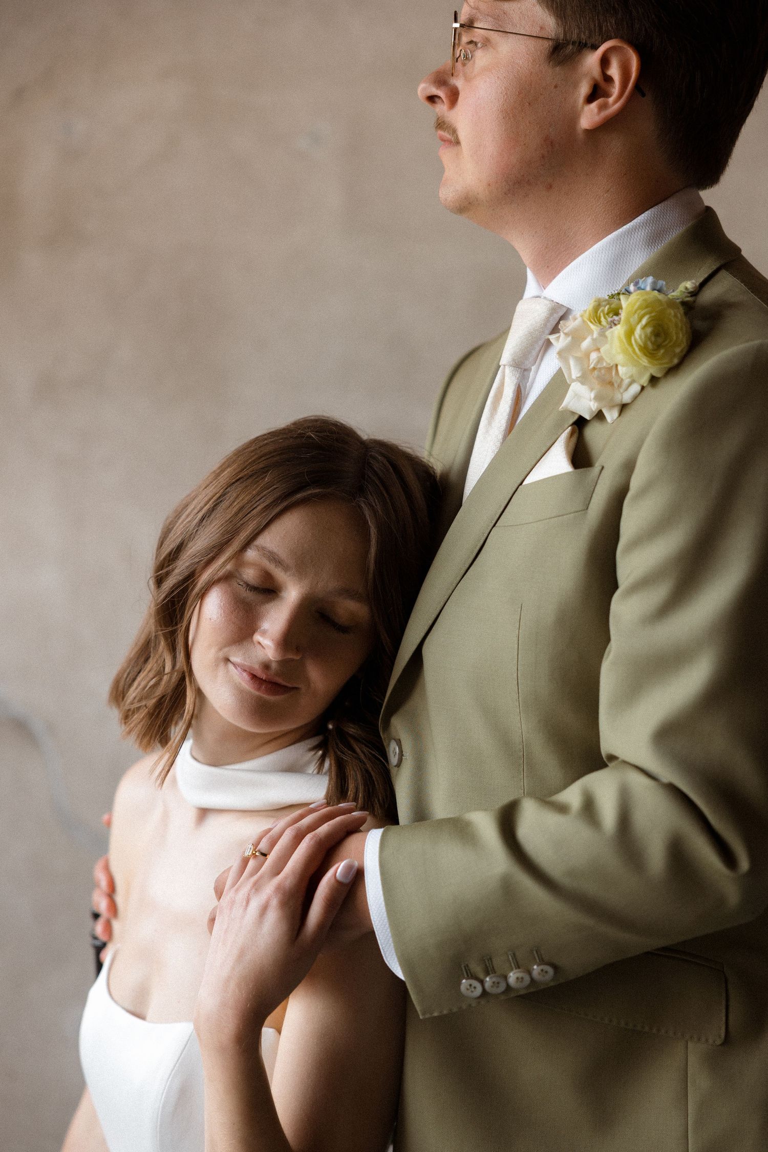 Intimate wedding portrait showing tender moments between newlyweds against neutral background.