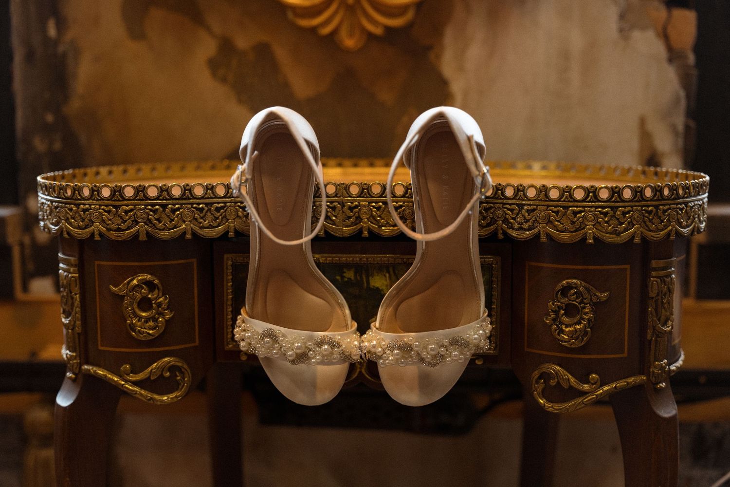 Vintage-style detail shot of ornate wedding shoes against decorative background.