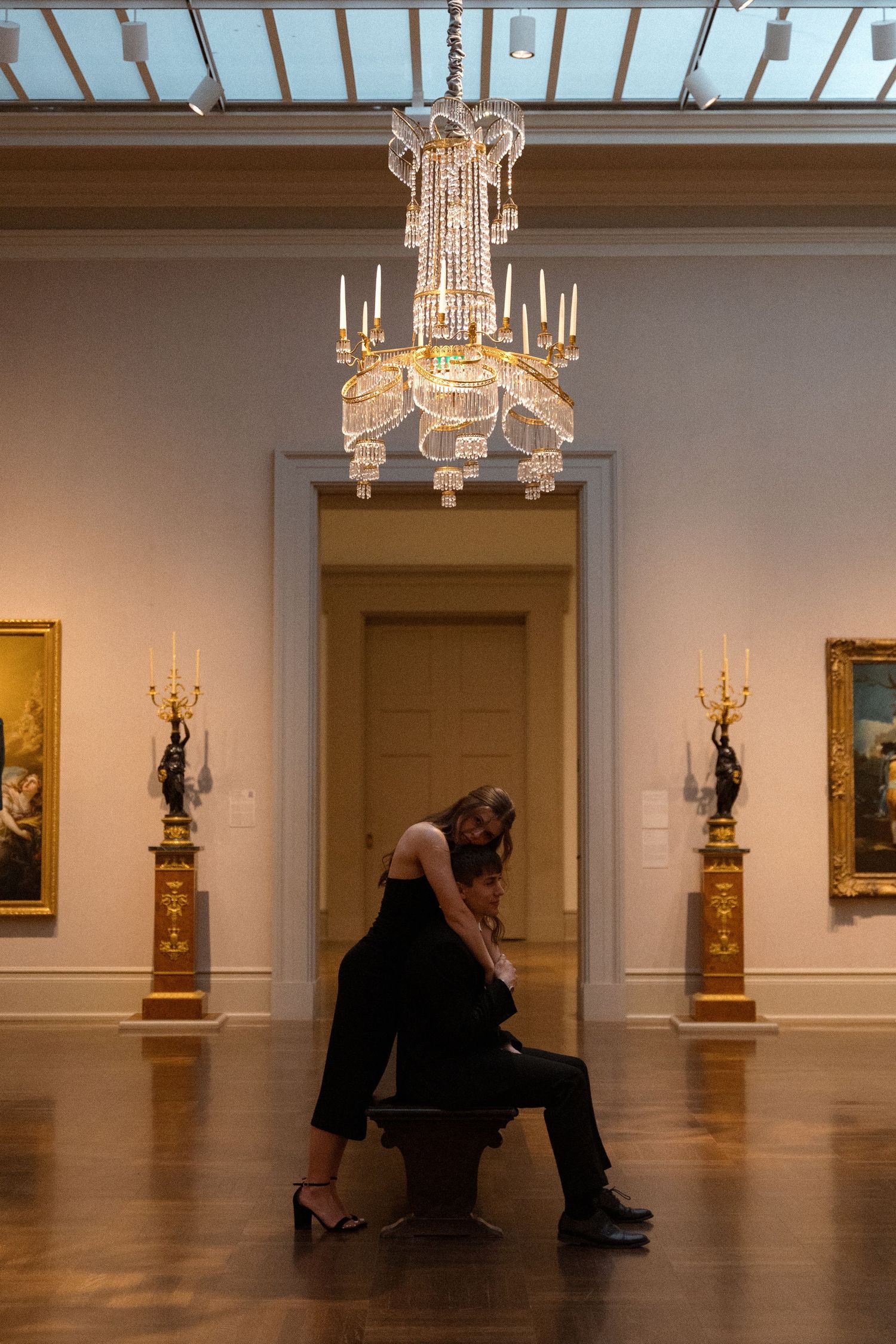 Dancers perform beneath crystal chandeliers in a spacious museum gallery.