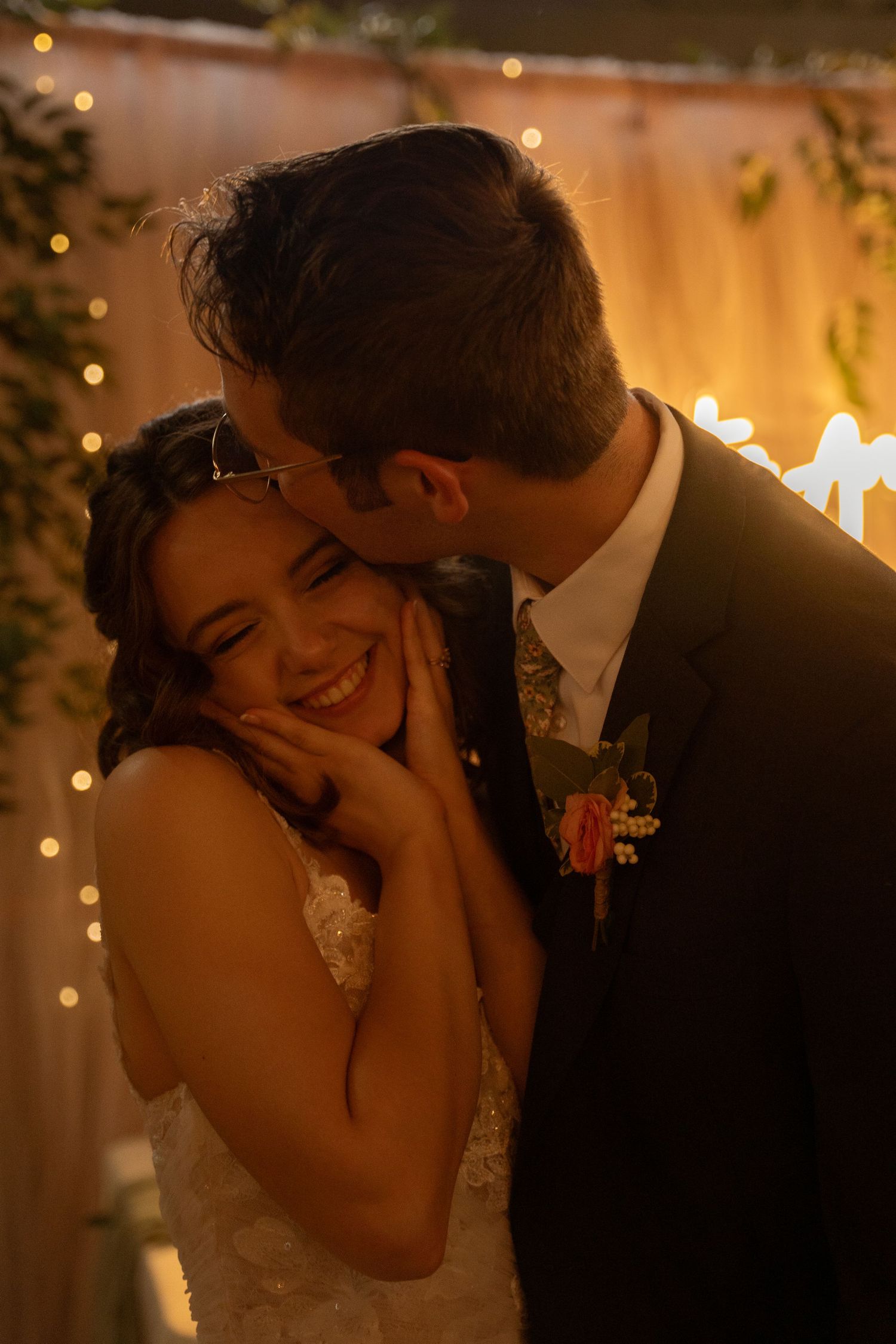 A romantic wedding moment captured with warm lighting and twinkling string lights in the background.
